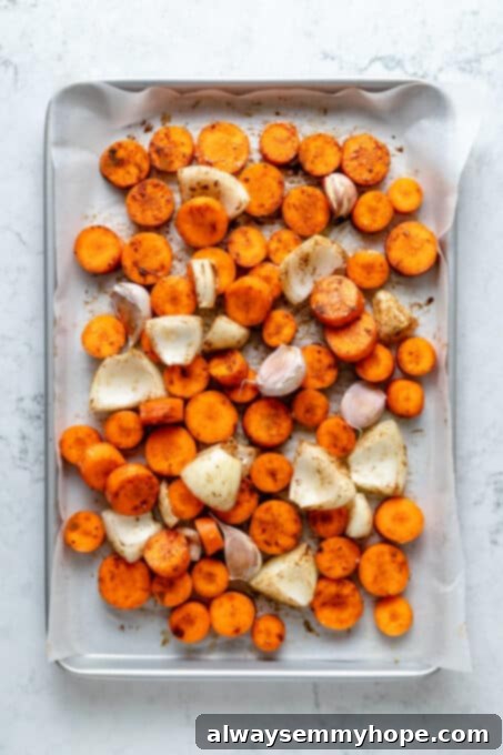 Golden Roasted Carrot Ginger Soup 5 Overhead view of carrots, onions, and garlic on parchment-lined sheet pan
