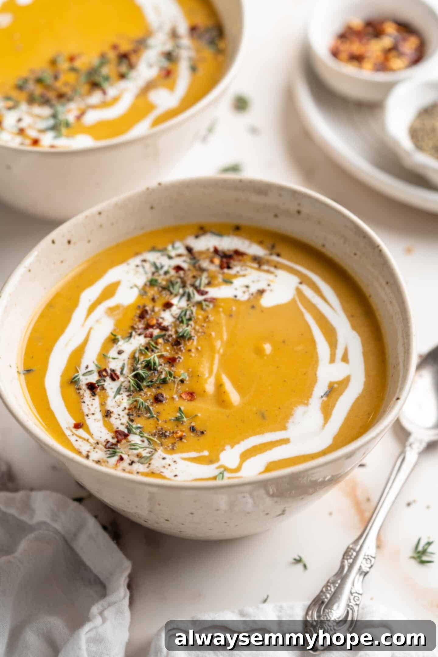 Garnished Butternut Squash Soup with Coconut Milk and Herbs Bowl of vegan butternut squash soup with swirl of coconut milk, fresh thyme, and red pepper flakes for garnish, viewed from above