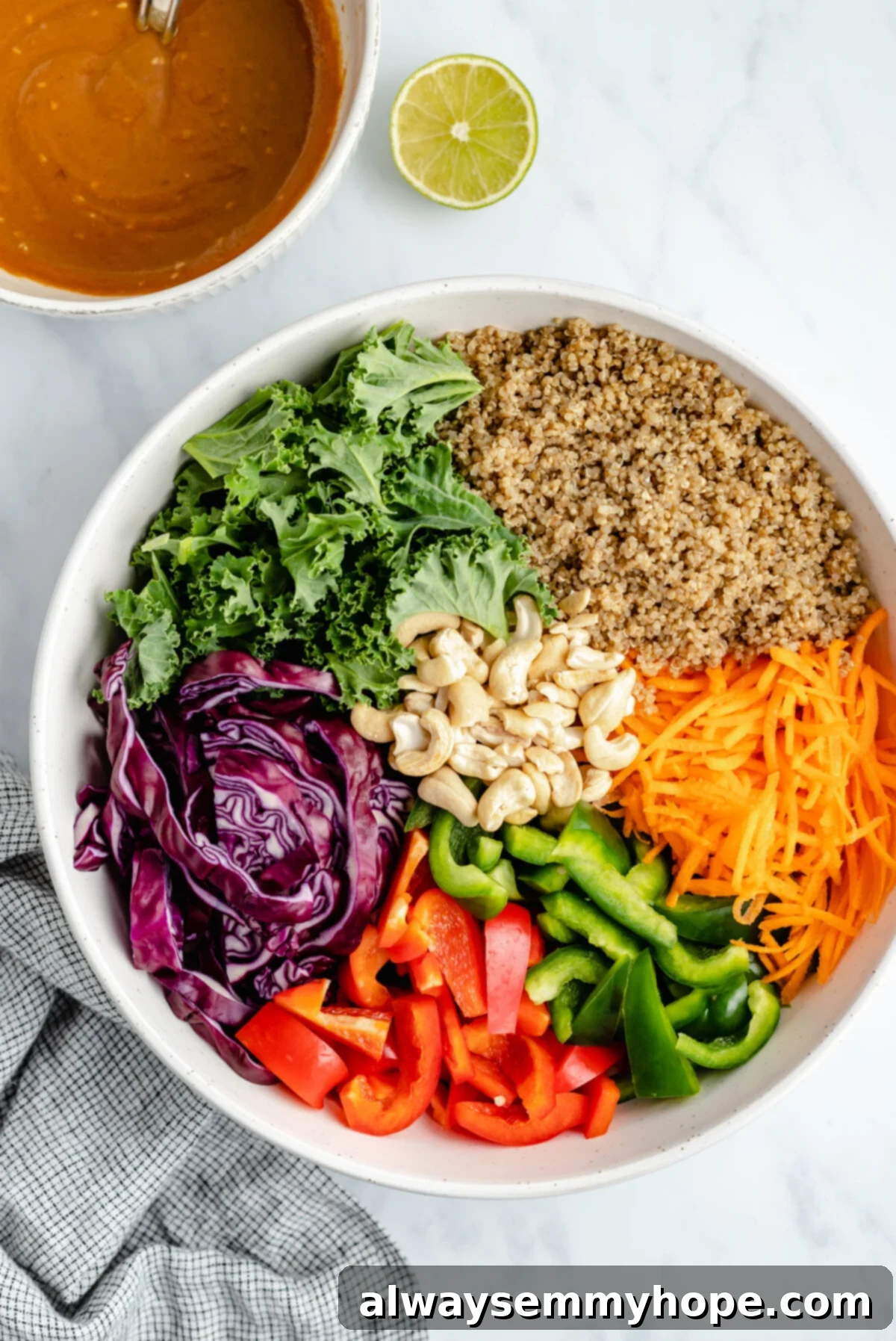 Explore the fresh ingredients for a quick and flavorful Thai quinoa salad, featuring a rich peanut ginger dressing for a perfect vegan meal. A collection of fresh, vibrant Thai quinoa salad ingredients, including colorful bell peppers, kale, carrots, red cabbage, cooked quinoa, and cashews, artfully arranged around a small bowl of creamy peanut ginger dressing.