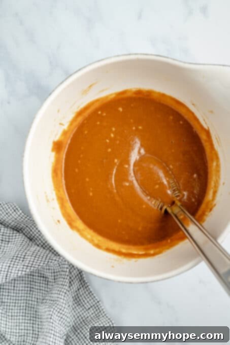 Prepare the flavorful peanut ginger dressing by whisking ingredients together until smooth, perfect for your easy Thai quinoa salad. Close-up shot of creamy peanut ginger dressing being whisked together in a small bowl, showcasing its smooth texture.
