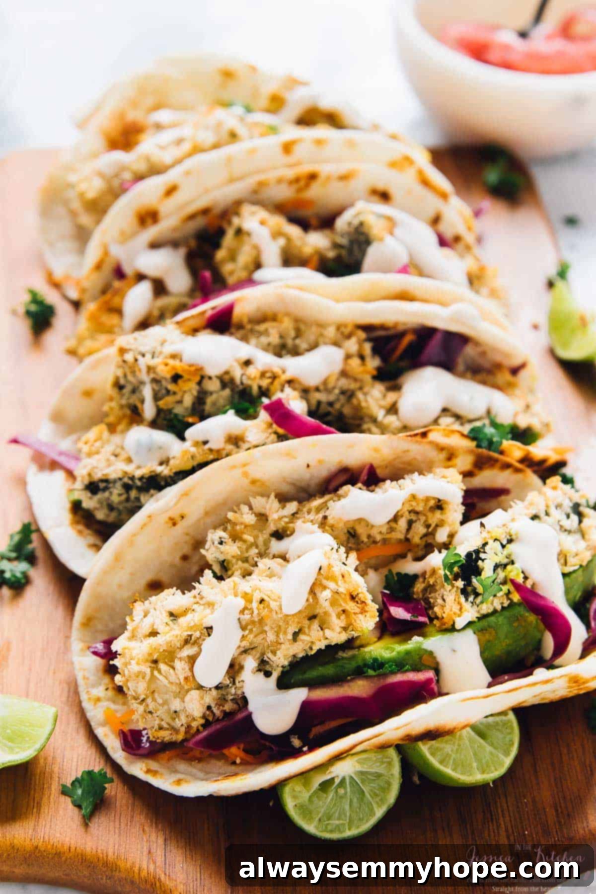 Four crispy zucchini tacos lined up on a rustic cutting board, garnished with fresh herbs and lime wedges.
