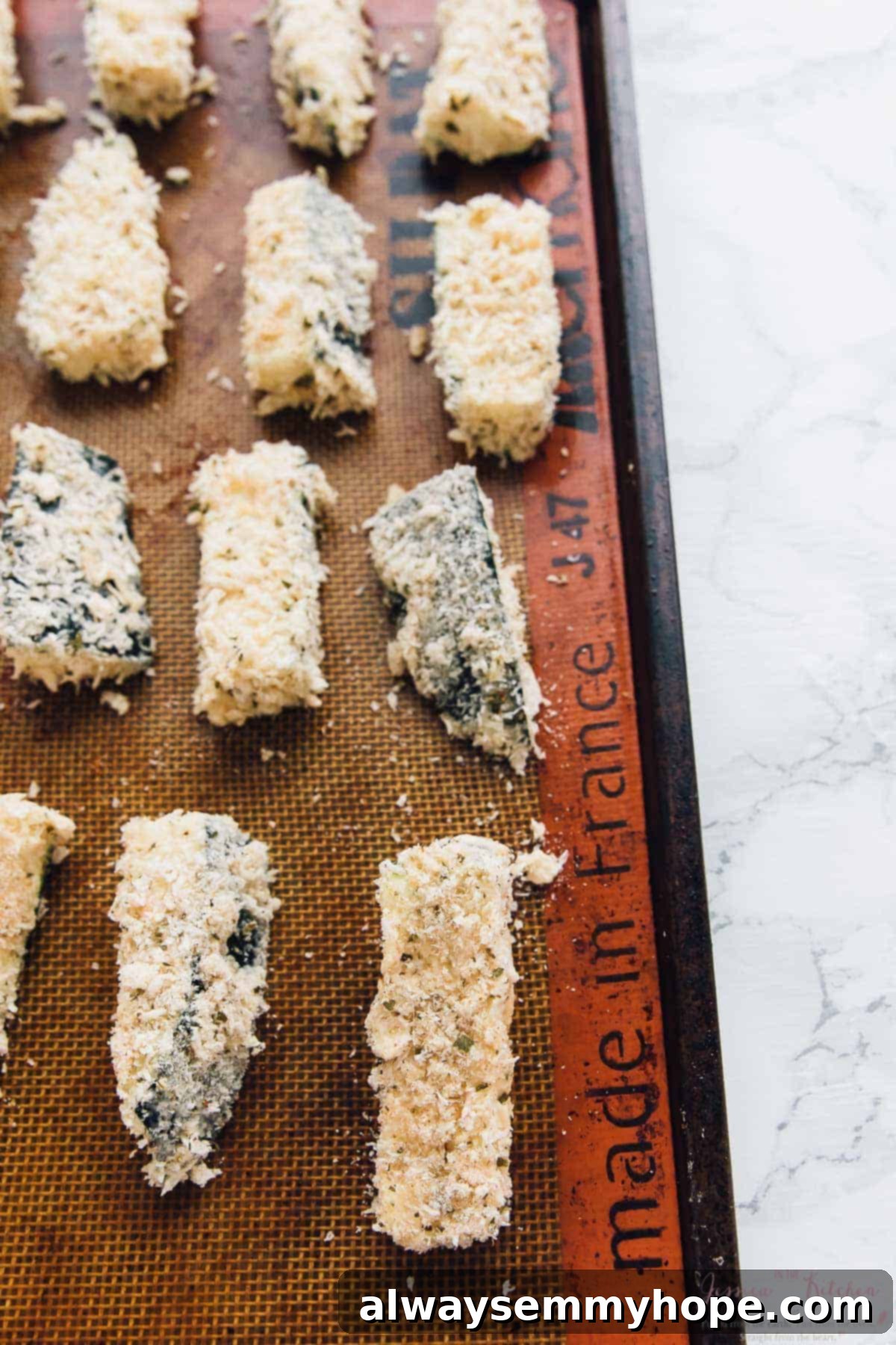 Crispy breaded zucchini pieces arranged neatly on a silpat-lined baking sheet, ready for oven baking.