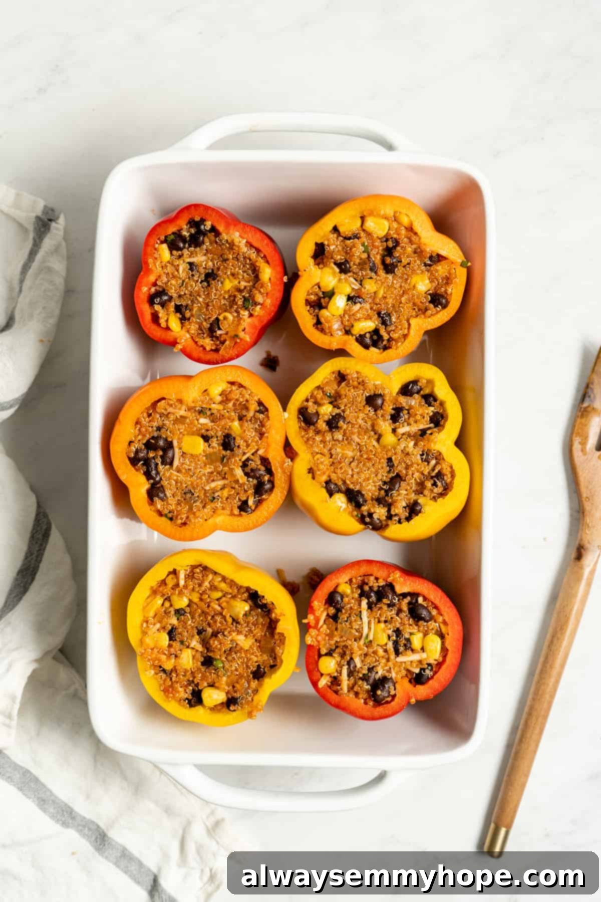Hollowed bell peppers generously stuffed with the savory quinoa, black bean, and corn mixture in a baking dish.