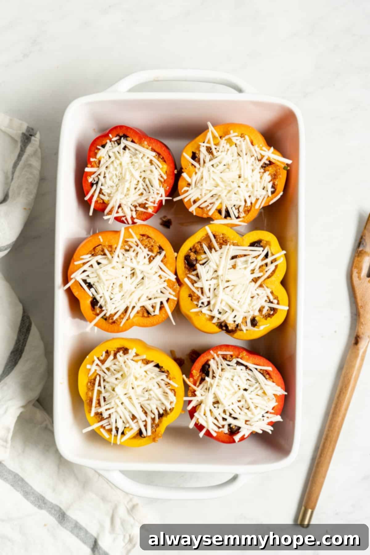 Stuffed bell peppers in a baking dish, generously topped with vegan mozzarella cheese, ready for baking.