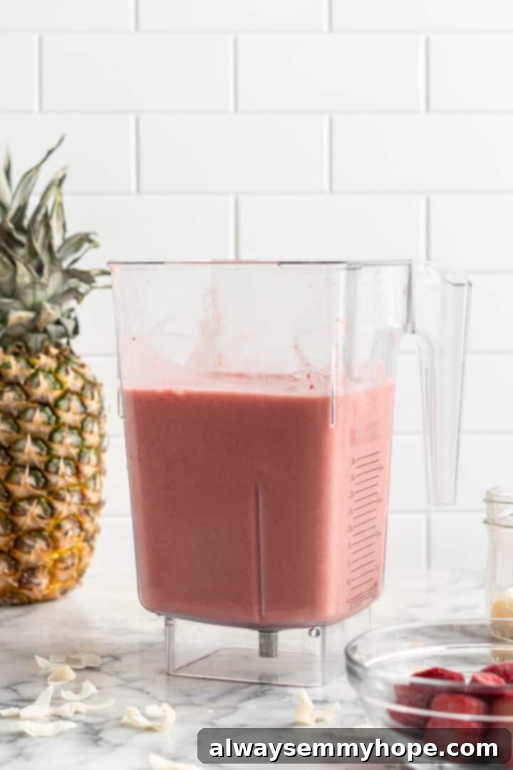 This vegan strawberry pineapple smoothie is light, refreshing, and ready to drink in just 5 minutes. You only need 3 ingredients to make it! Close-up shot of a creamy strawberry pineapple smoothie actively blending in a high-speed blender, showing its smooth and vibrant texture.