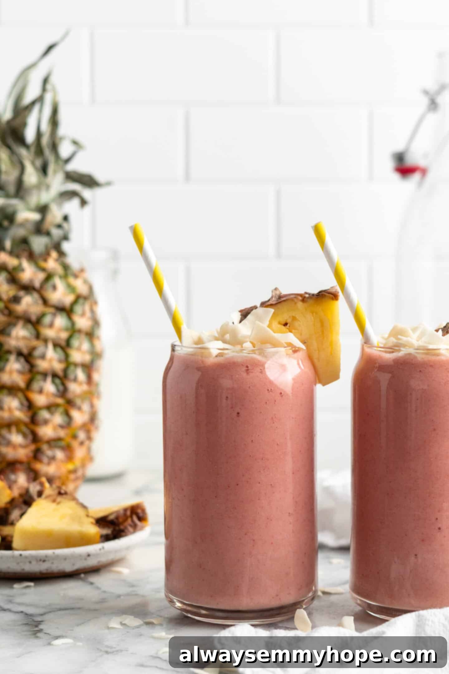 This vegan strawberry pineapple smoothie is light, refreshing, and ready to drink in just 5 minutes. You only need 3 ingredients to make it! Two glasses of refreshing strawberry pineapple smoothie, garnished with toasted coconut flakes and fresh pineapple wedges, ready to be enjoyed.
