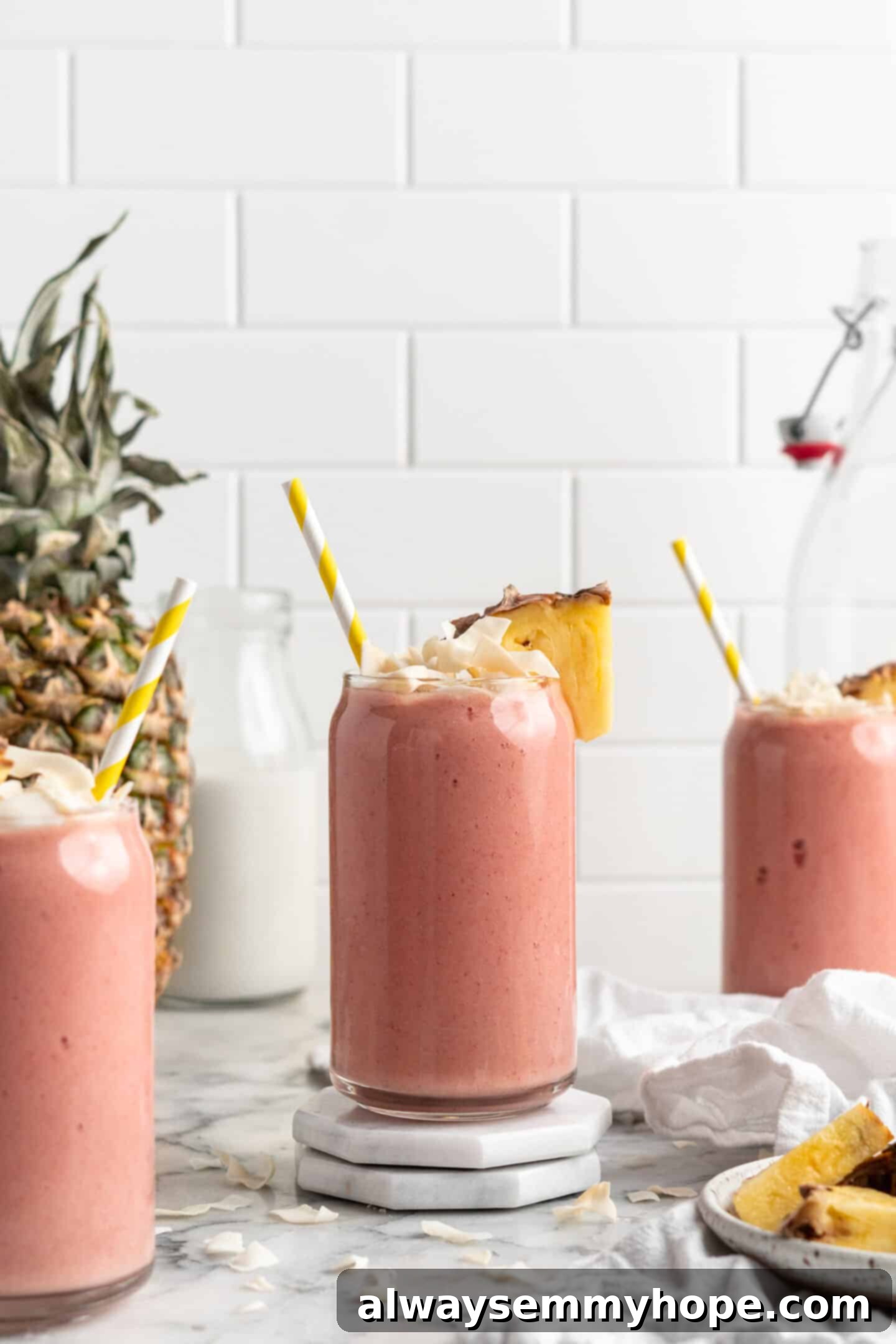 This vegan strawberry pineapple smoothie is light, refreshing, and ready to drink in just 5 minutes. You only need 3 ingredients to make it! Three perfectly blended strawberry pineapple smoothies in clear glasses with straws, adorned with fresh pineapple and toasted coconut, ready to serve.