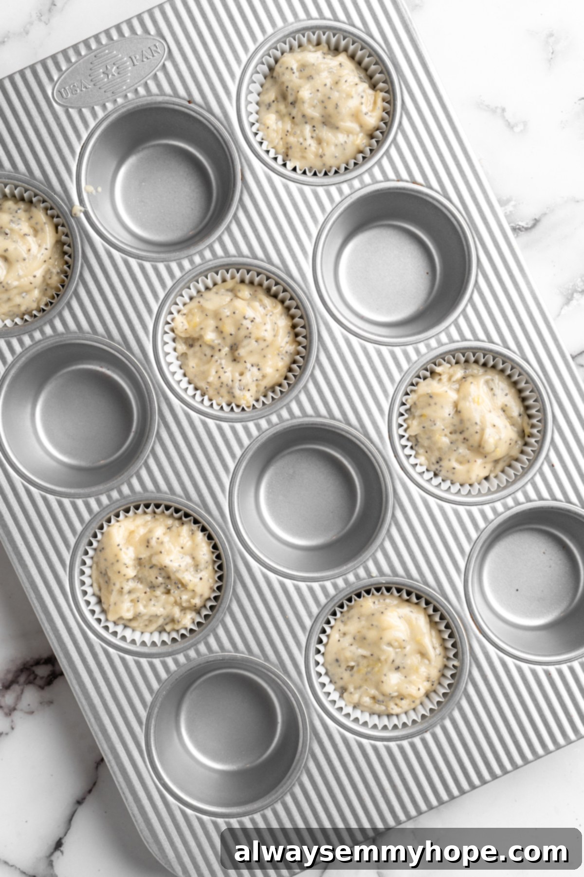 Vegan lemon poppyseed muffin batter scooped into a muffin pan, with one cup filled with water for even baking