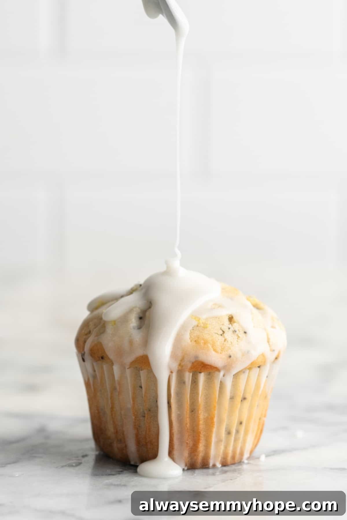 Close-up of a hand drizzling bright lemon glaze over a cooled vegan lemon poppyseed muffin on a wire rack