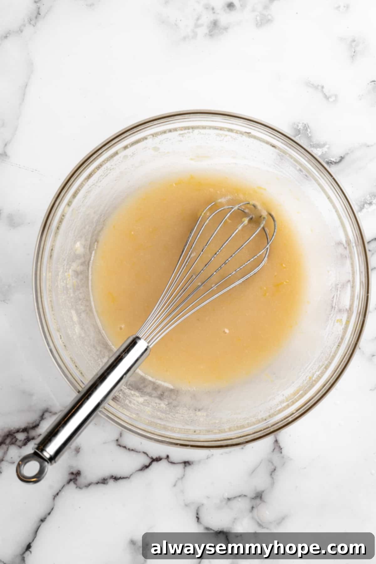 Overhead view of wet ingredients for vegan muffins being whisked in a glass mixing bowl, creating a smooth, emulsified mixture