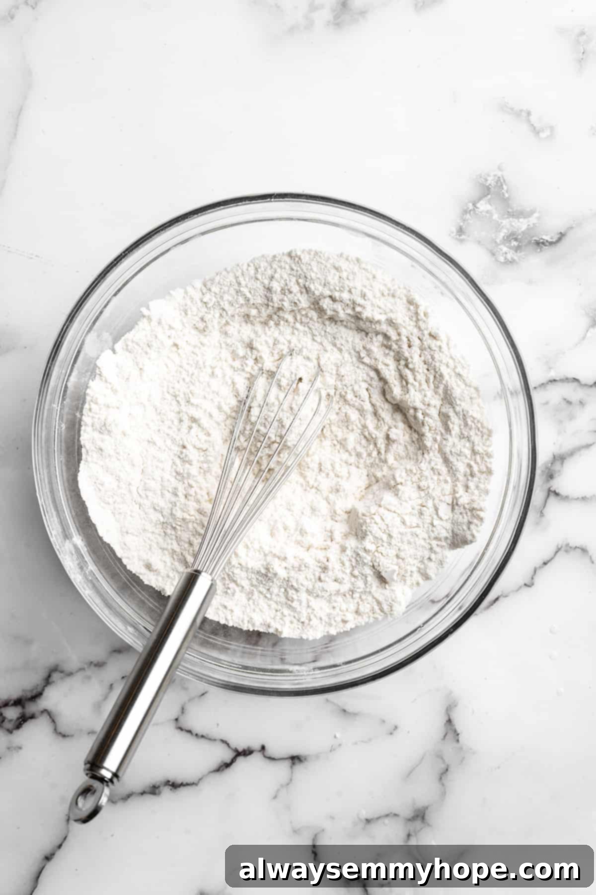 Overhead view of dry ingredients (flour, baking powder, salt) being whisked together in a separate small mixing bowl