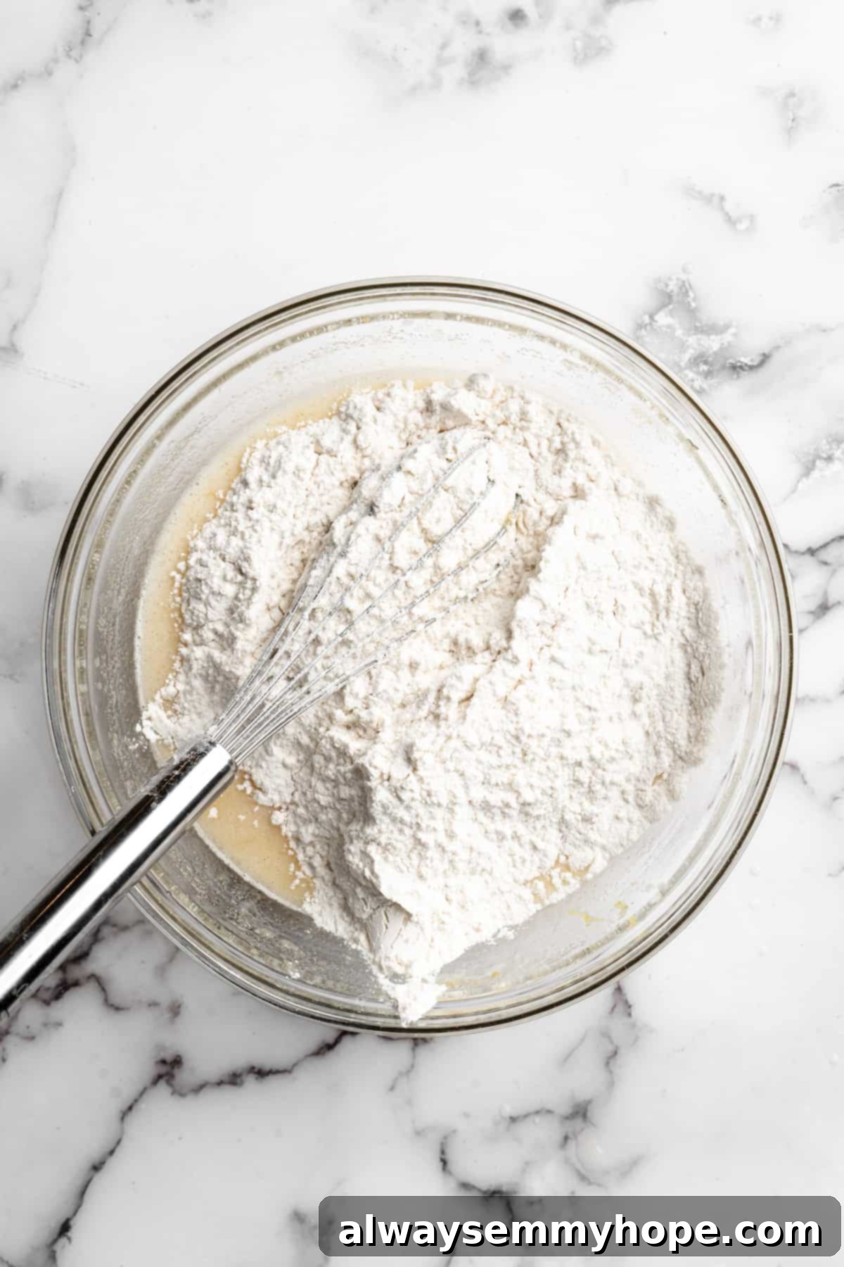 Overhead view of flour mixture being gently poured into the wet ingredients in a large mixing bowl for vegan muffins