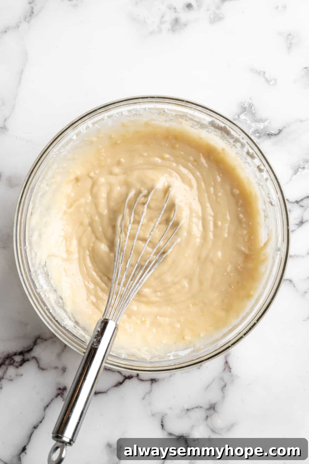 Overhead view of vegan lemon poppyseed muffin batter in a glass mixing bowl, showing its thick and creamy texture before adding poppyseeds