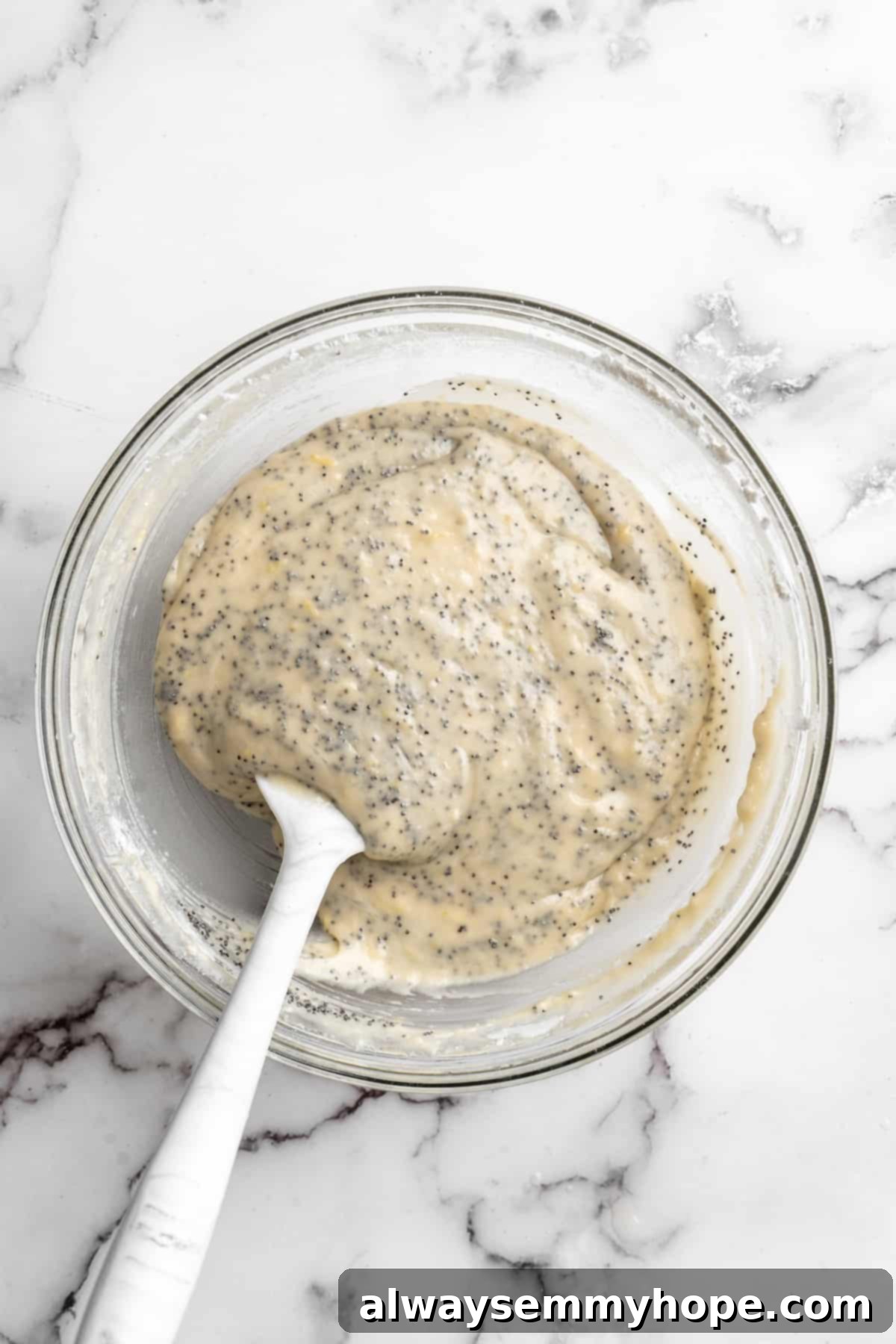 Overhead view of finished vegan lemon poppyseed muffin batter with poppyseeds evenly distributed in a glass mixing bowl