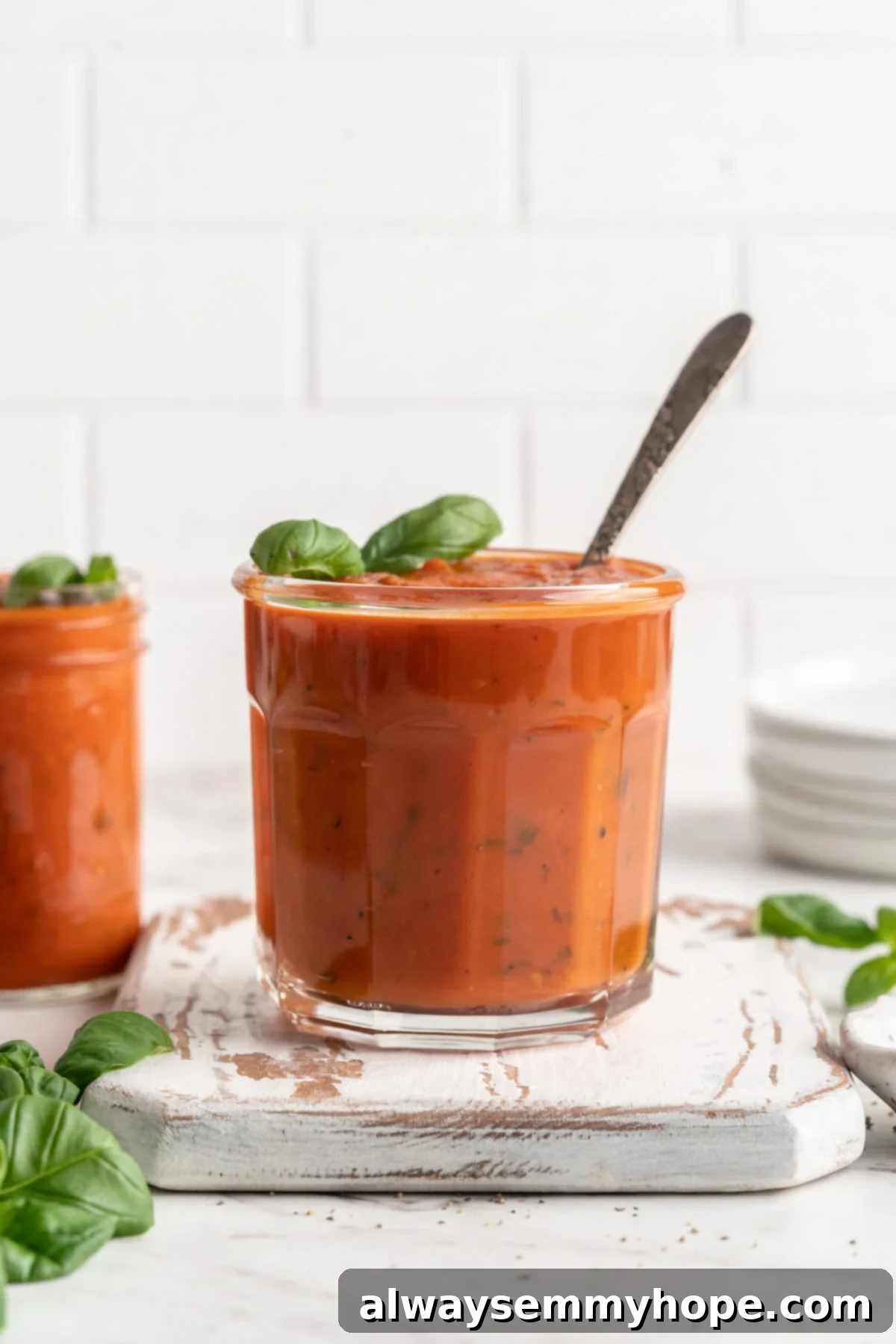 Discover the secret to amazing homemade tomato sauce with roasted garlic. It's versatile, great for meal prep, and freezer-friendly. Jar of flavorful homemade tomato sauce with a wooden spoon