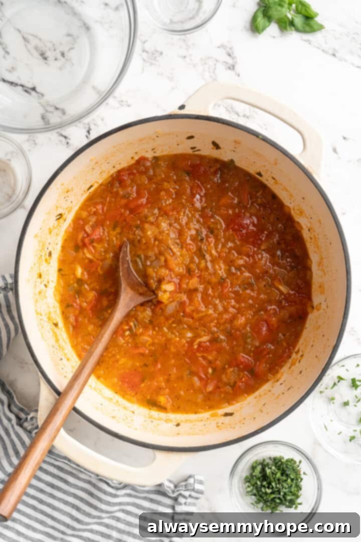 A close-up of the simmering homemade tomato sauce in a pot, its ingredients softened and flavors deepened before blending. Pot of homemade tomato sauce before pureeing, showing softened tomatoes and herbs