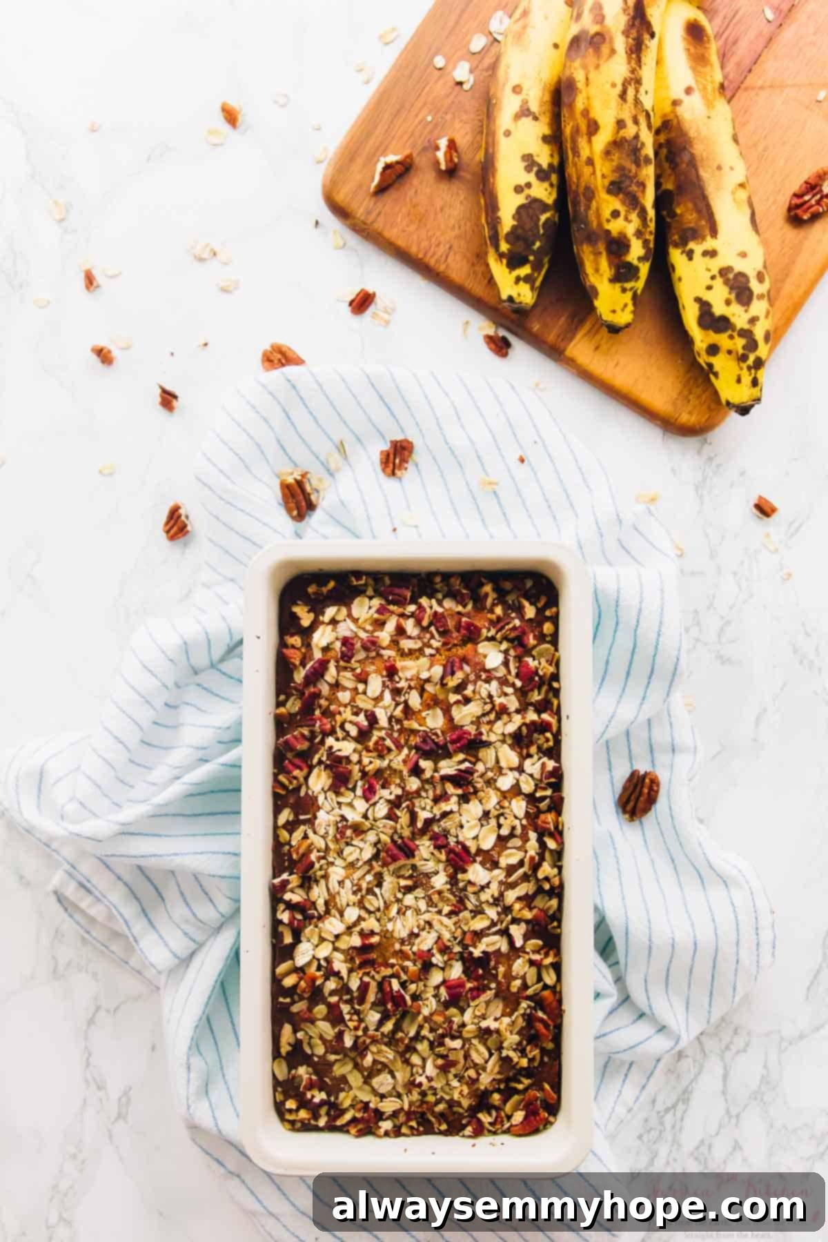 This is the best gluten-free vegan banana bread! Soft, moist, and easy to make with simple ingredients. Enjoy it with your favorite mix-ins! Overhead view of gluten-free vegan banana bread in loaf pan with bananas on cutting board in background