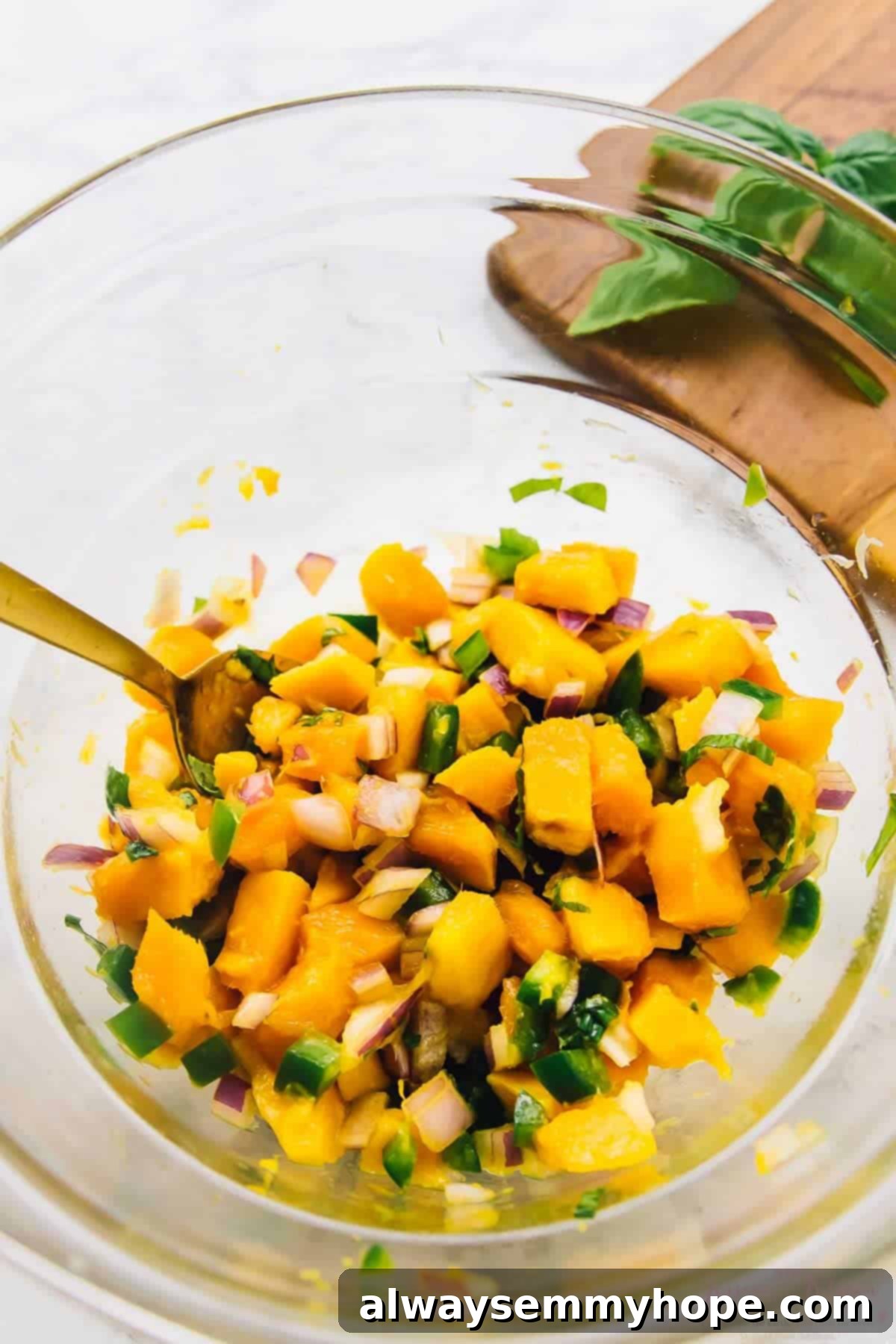 Freshly prepared mango basil salsa mixed in a glass bowl with a spoon, showing its chunky texture and vibrant colors.