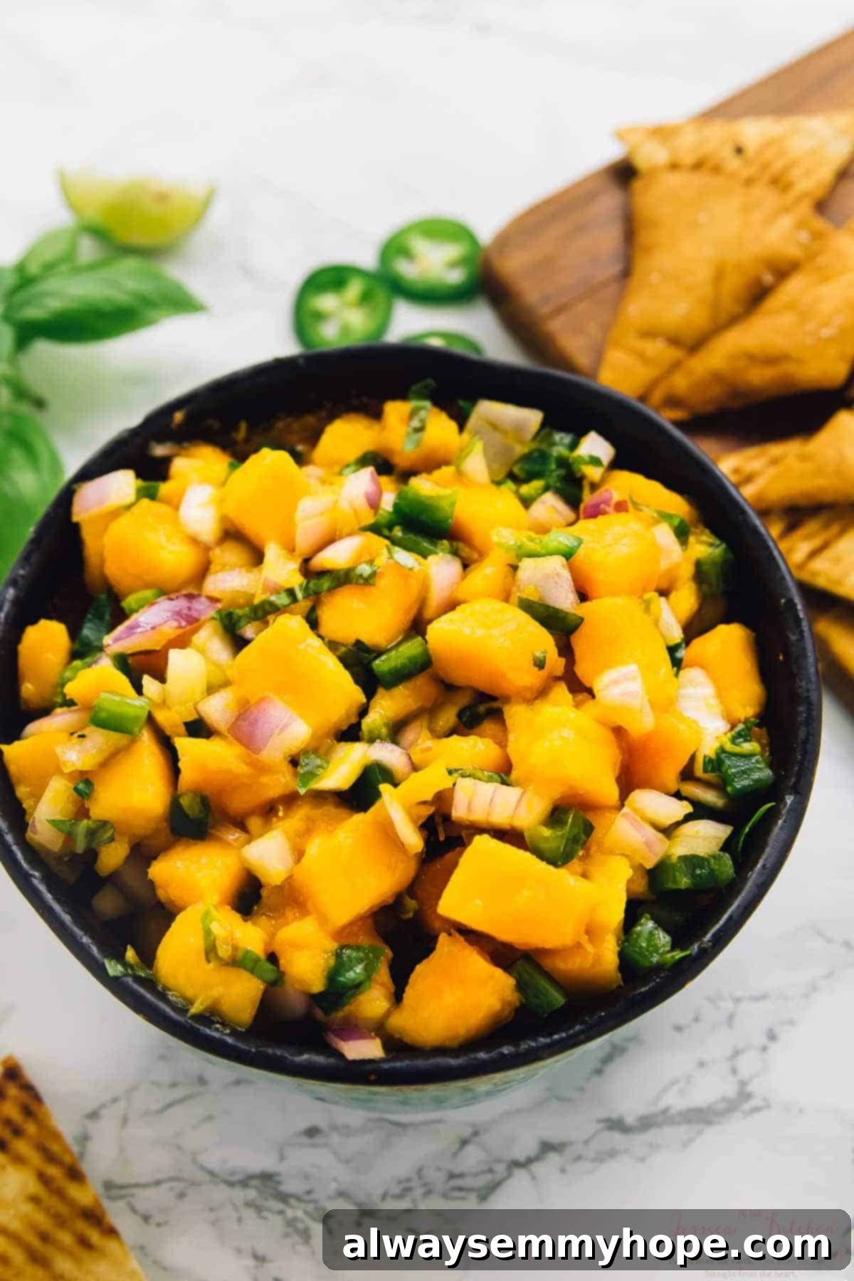 A bowl of vibrant mango basil salsa served with golden pita chips, highlighting a perfect party appetizer.