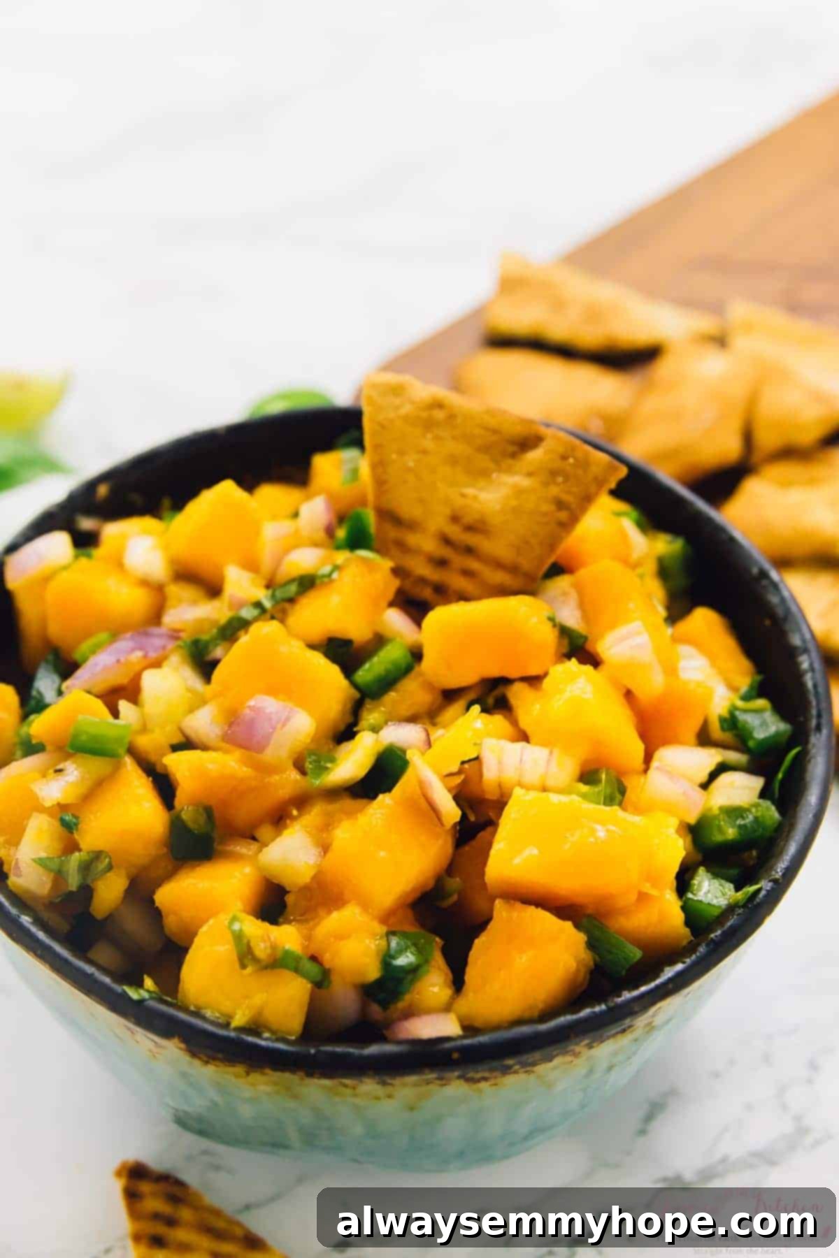 Close-up of a bowl of mango basil salsa with a single pita chip dipped in, showcasing the perfect texture for dipping.