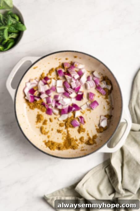 Effortless Thai Green Curry 5 Red onion and curry paste sizzling in a pan, releasing their aromatic flavors.