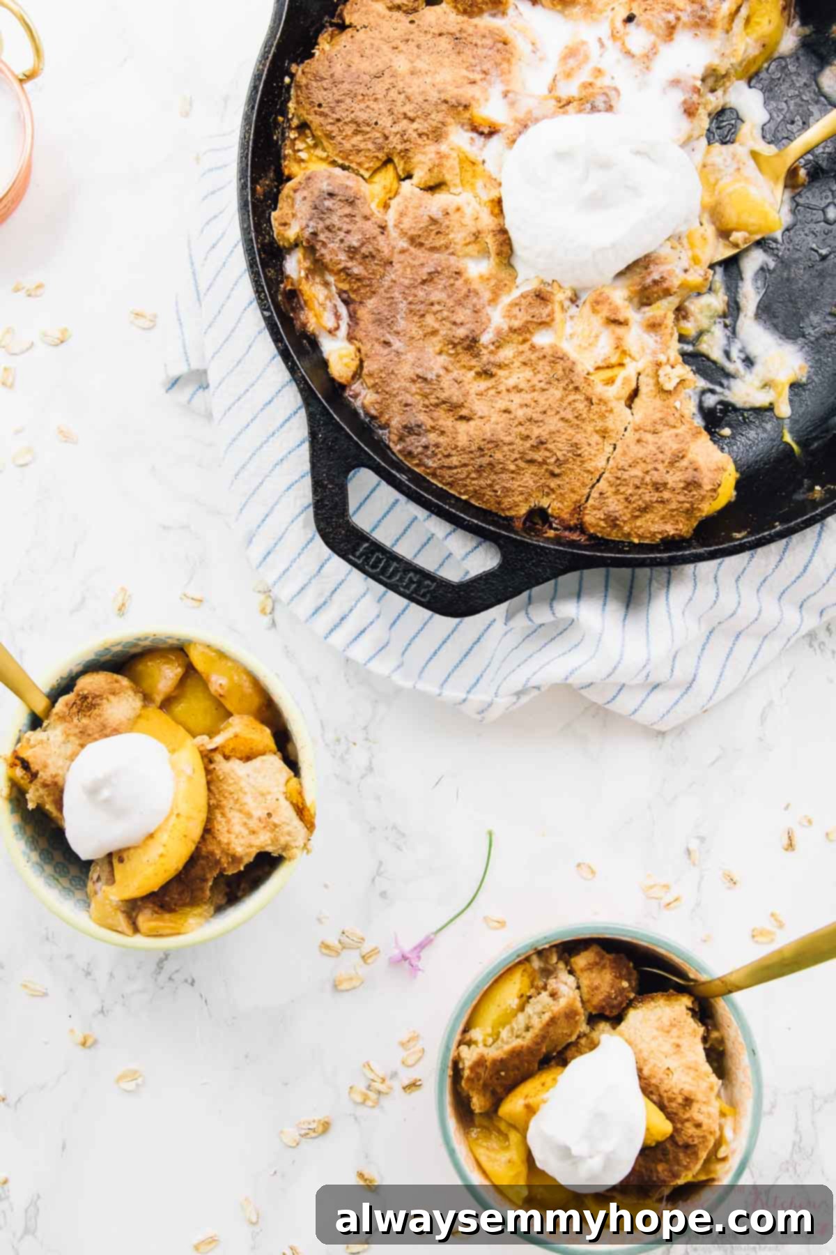 Overhead shot of warm breakfast peach cobbler in a black skillet with a dollop of coconut cream on top, and two smaller portions in bowls beside it.