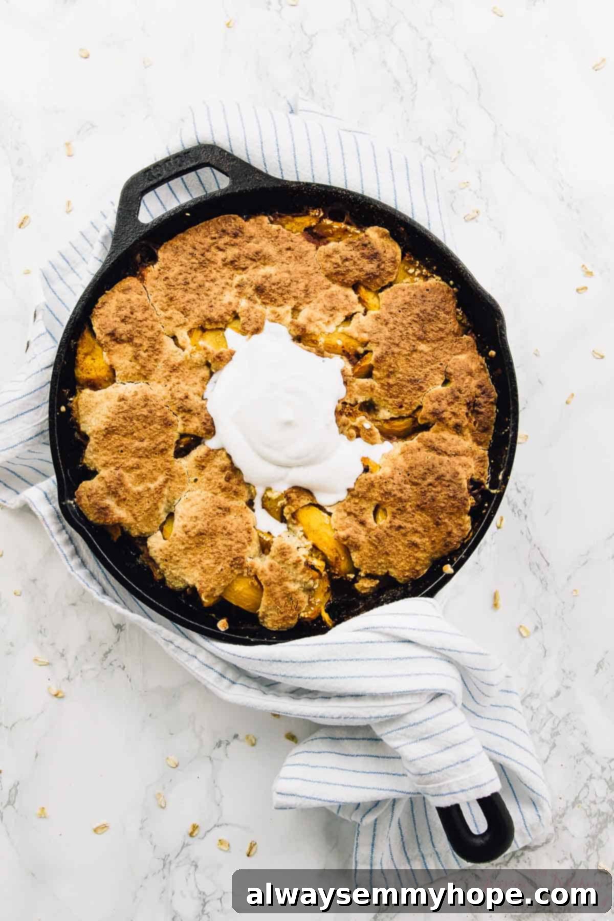 Overhead view of breakfast peach cobbler in skillet, beautifully topped with a swirl of coconut cream.