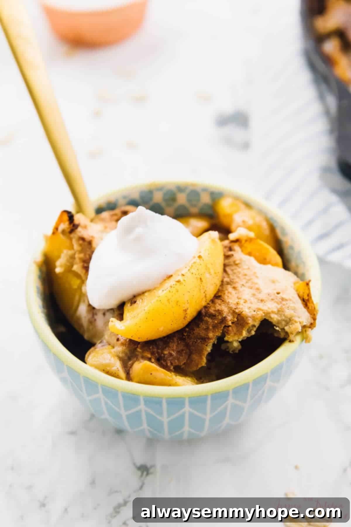 A small bowl of breakfast peach cobbler with a dollop of coconut cream on top, ready to be enjoyed.