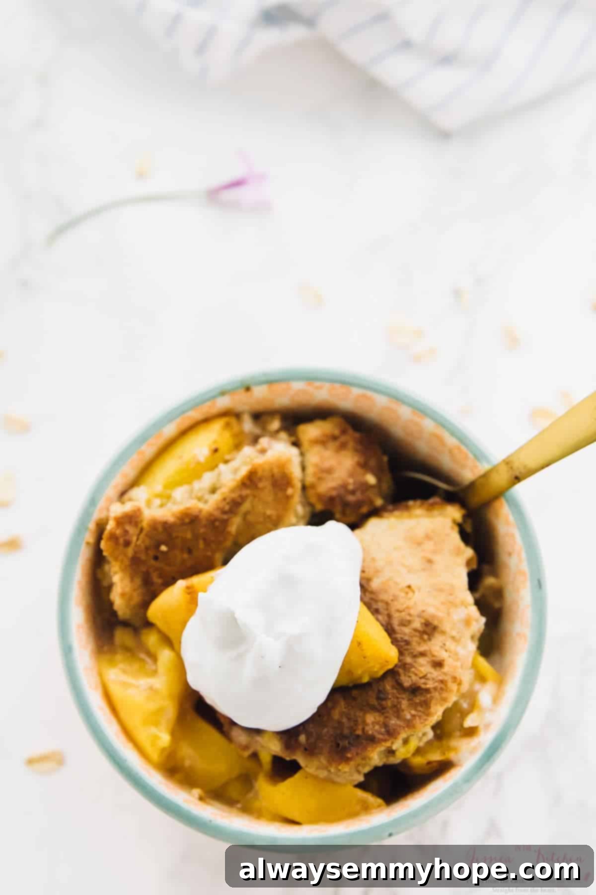 Overhead view of a small bowl of breakfast peach cobbler with a dollop of coconut cream, artfully arranged.