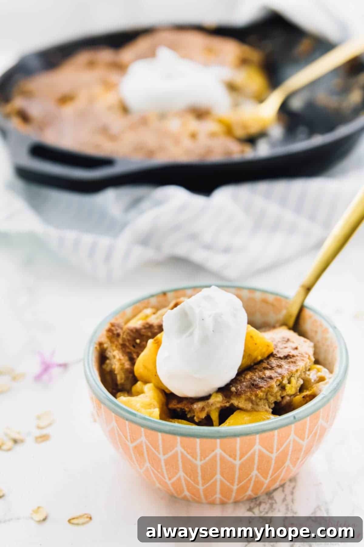 A small bowl of vegan breakfast peach cobbler in the foreground, with a large skillet of cobbler in the background.
