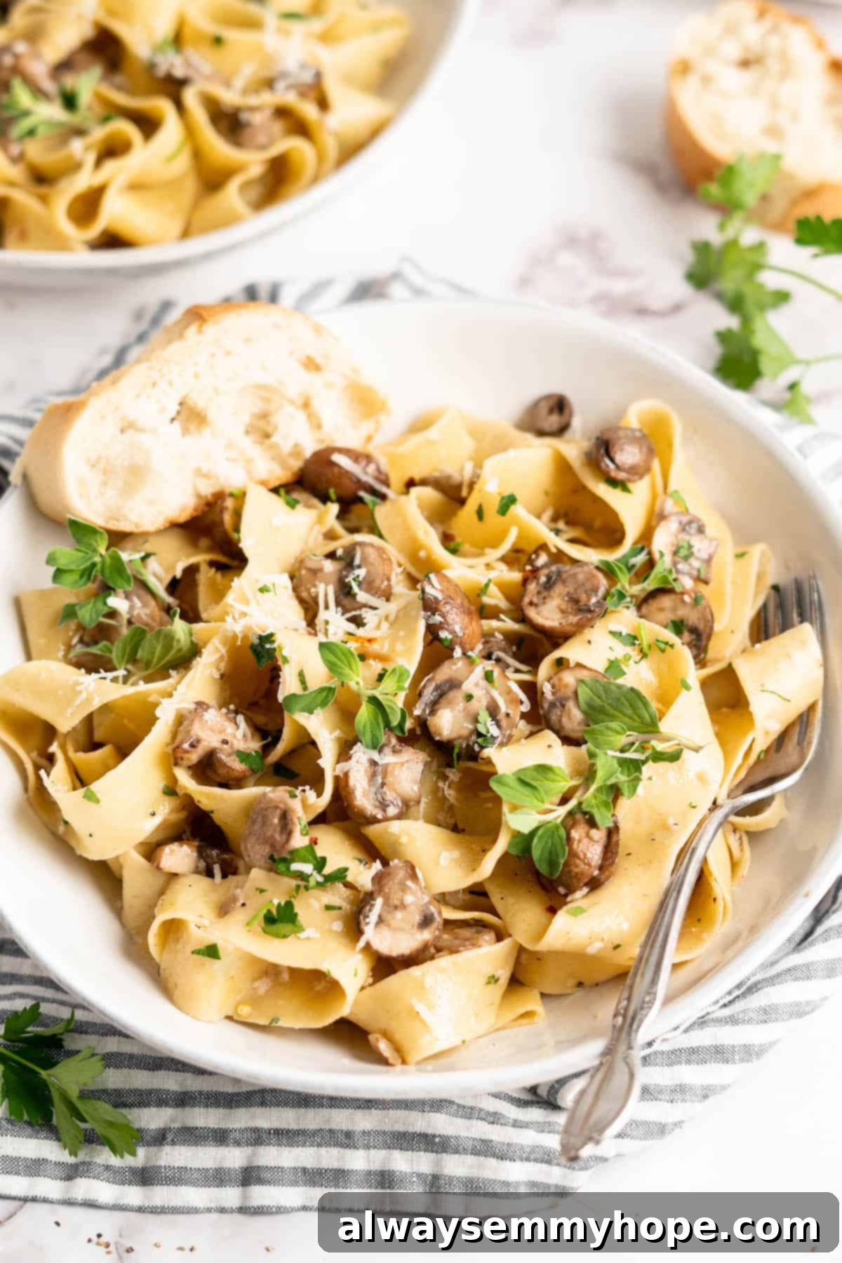 Creamy Garlic Mushroom Pasta served in a white bowl with a fork and a slice of bread, showcasing a close-up of the delicious dish.