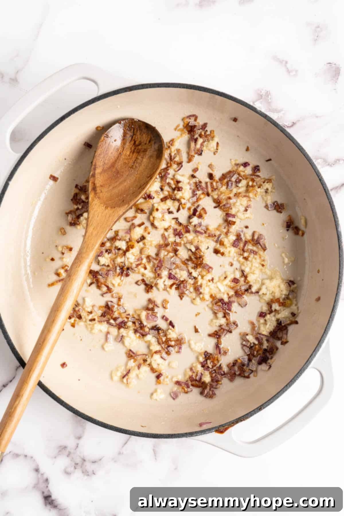 Overhead view of onions and garlic in a pan with a wooden spoon, perfectly sautéing.