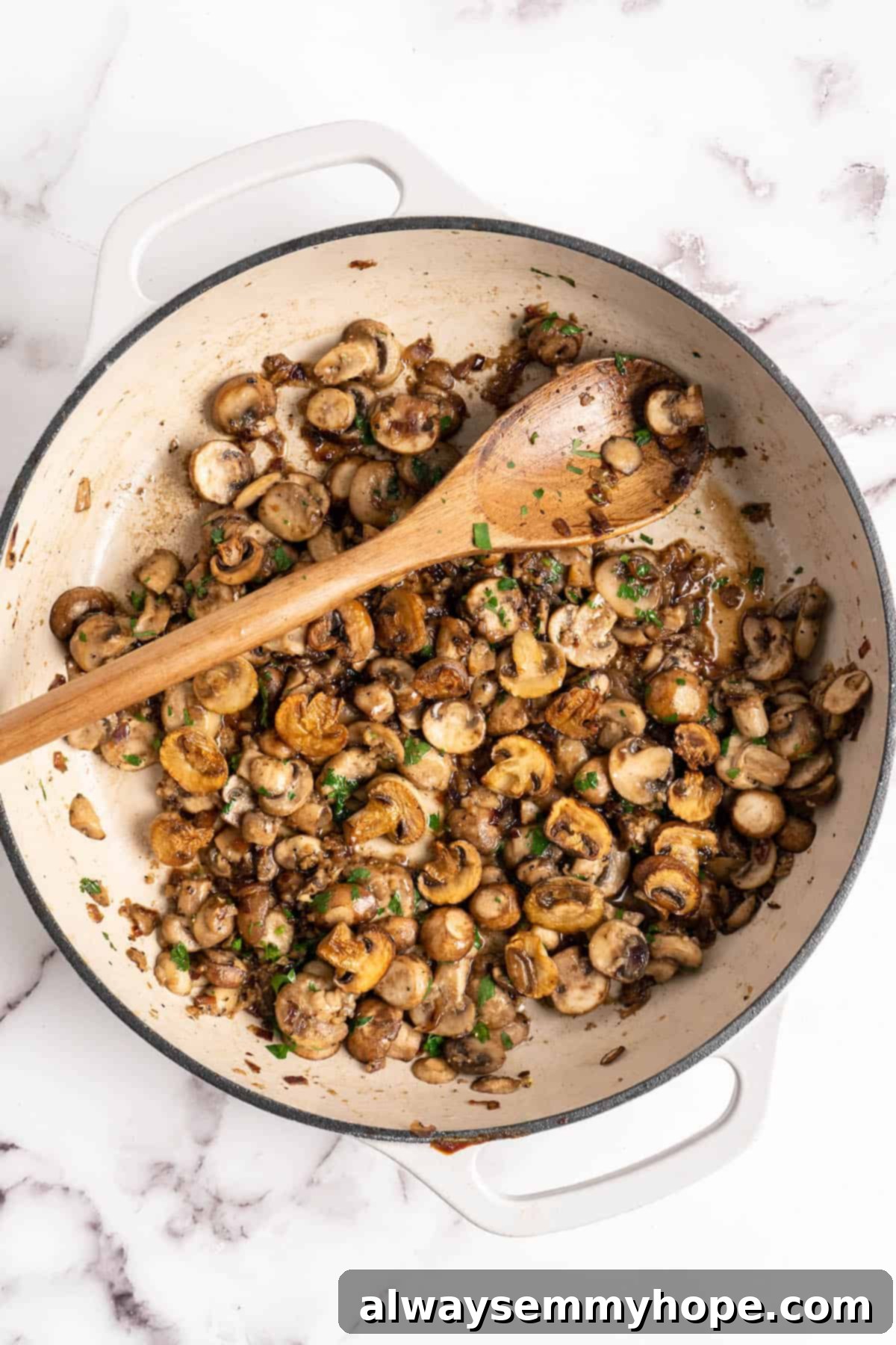 Overhead view of perfectly cooked mushrooms in a pan with a wooden spoon, showing rich caramelization.