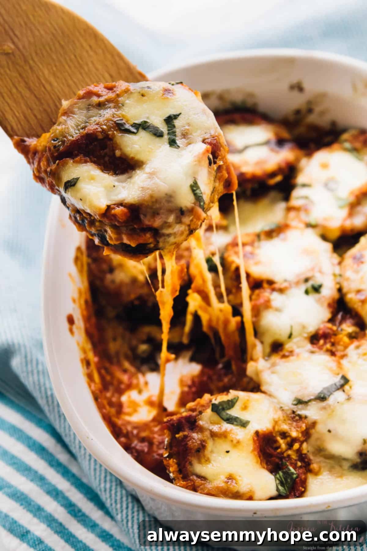 Baked eggplant scooped out of a baking dish with a spatula, showcasing tender slices and melted vegan cheese