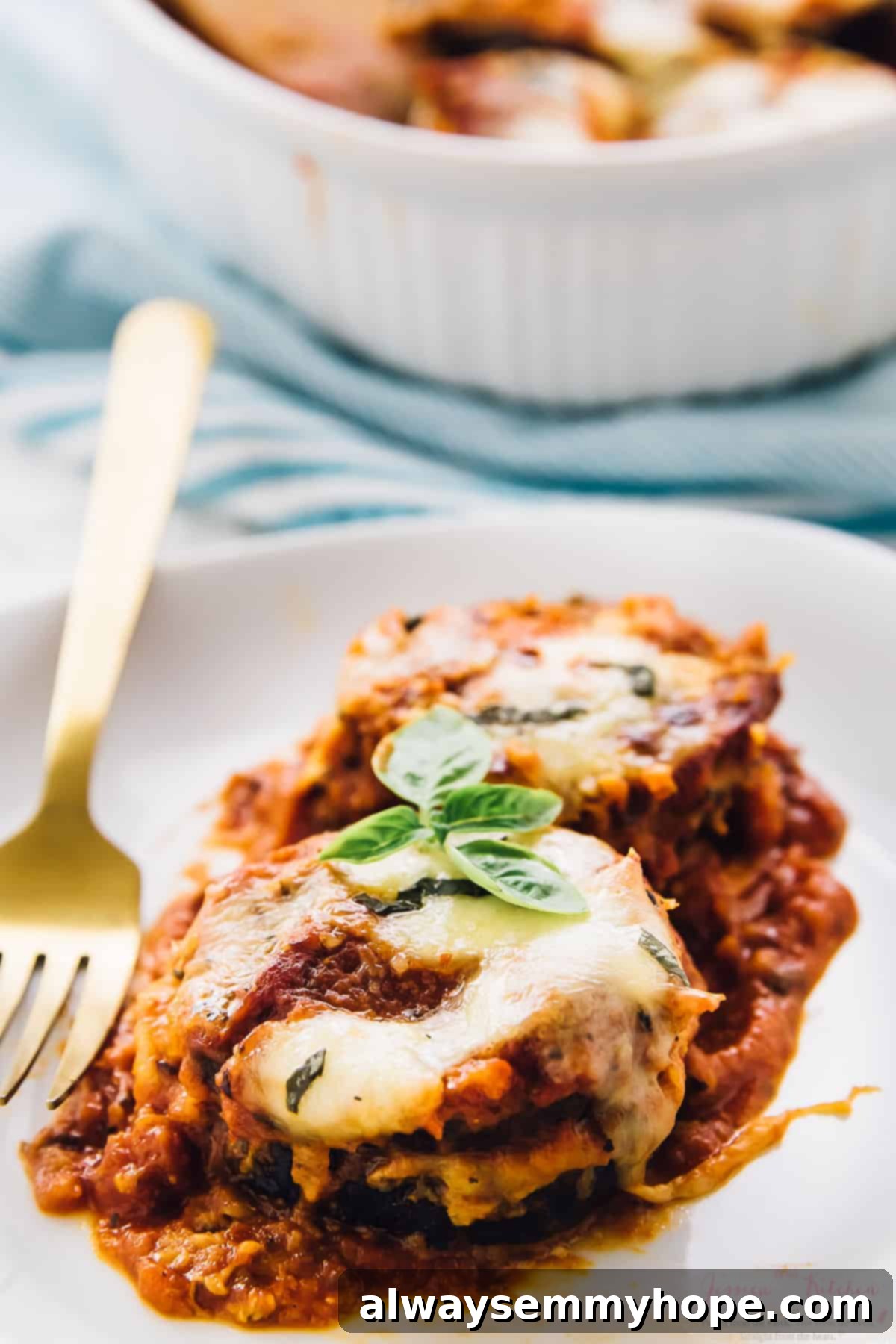 A serving of Baked Eggplant Parmesan on a white plate with a gold fork, garnished with fresh basil.