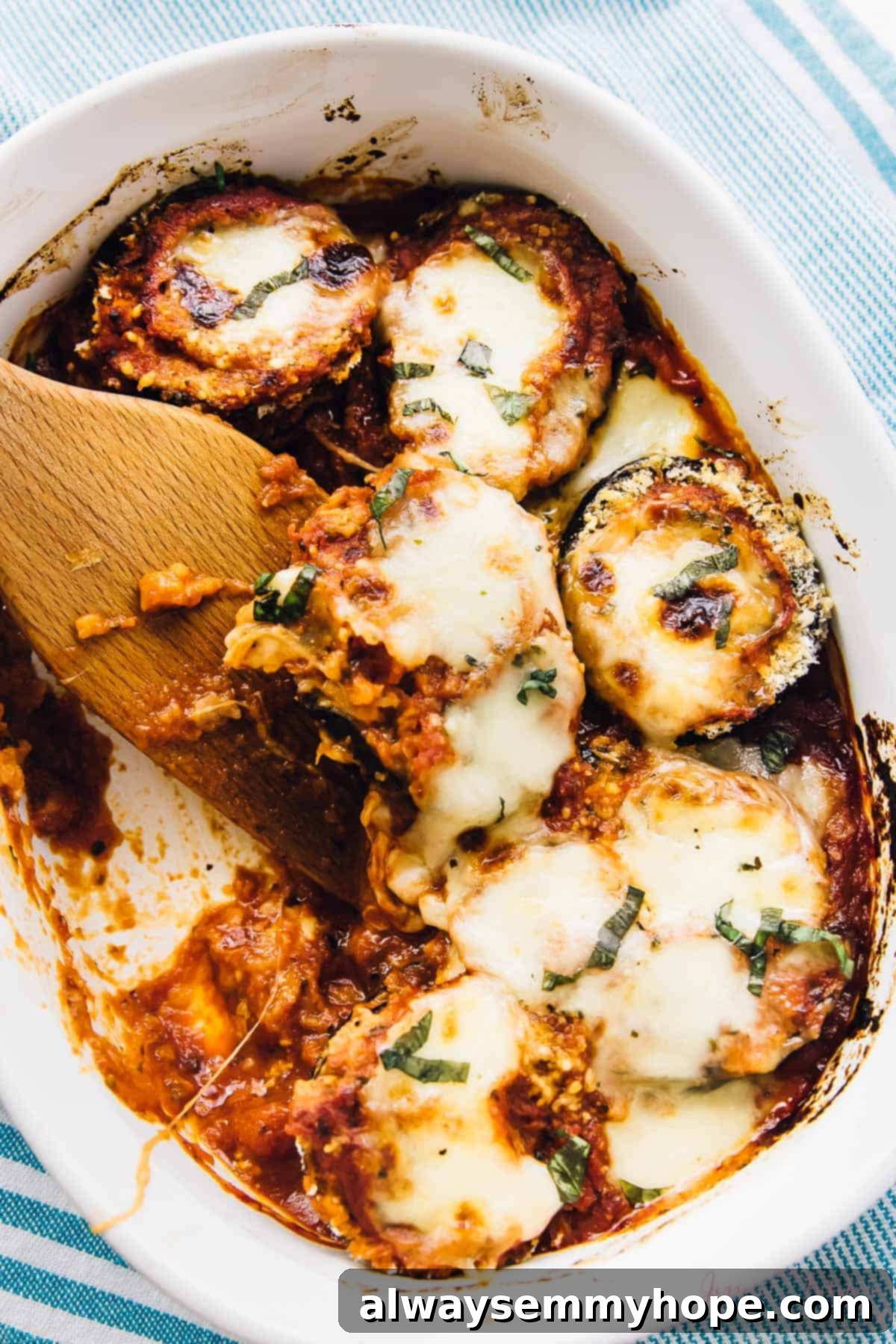 A spatula digging into a baking dish of Baked Eggplant Parmesan, revealing layers of eggplant, sauce, and cheese.