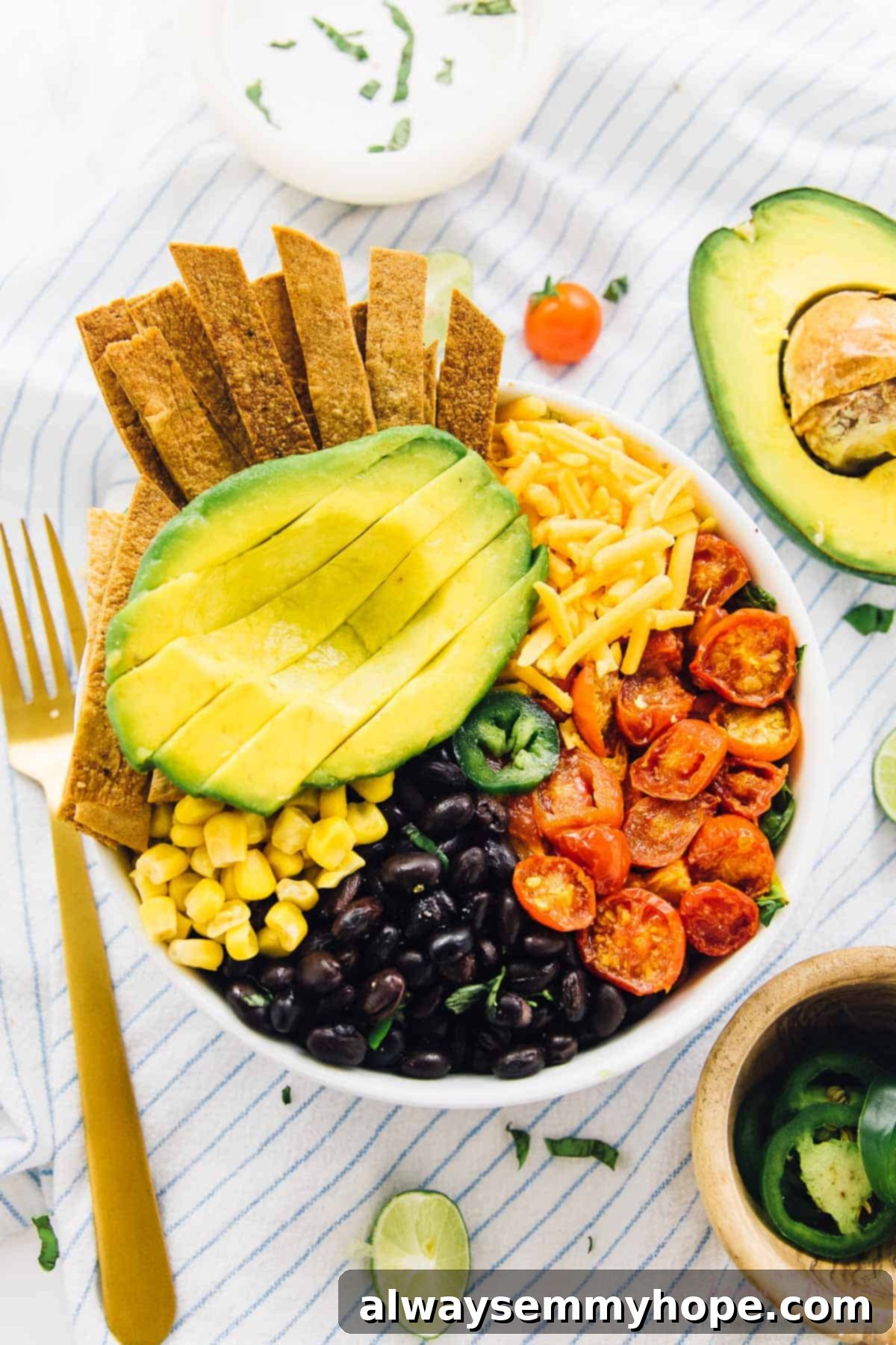 Loaded Taco Salad Bowl with Fresh Lime Crema Drizzle 2 Top down shot of taco bowl on a striped cloth with a bowl of jalapenos on the side.