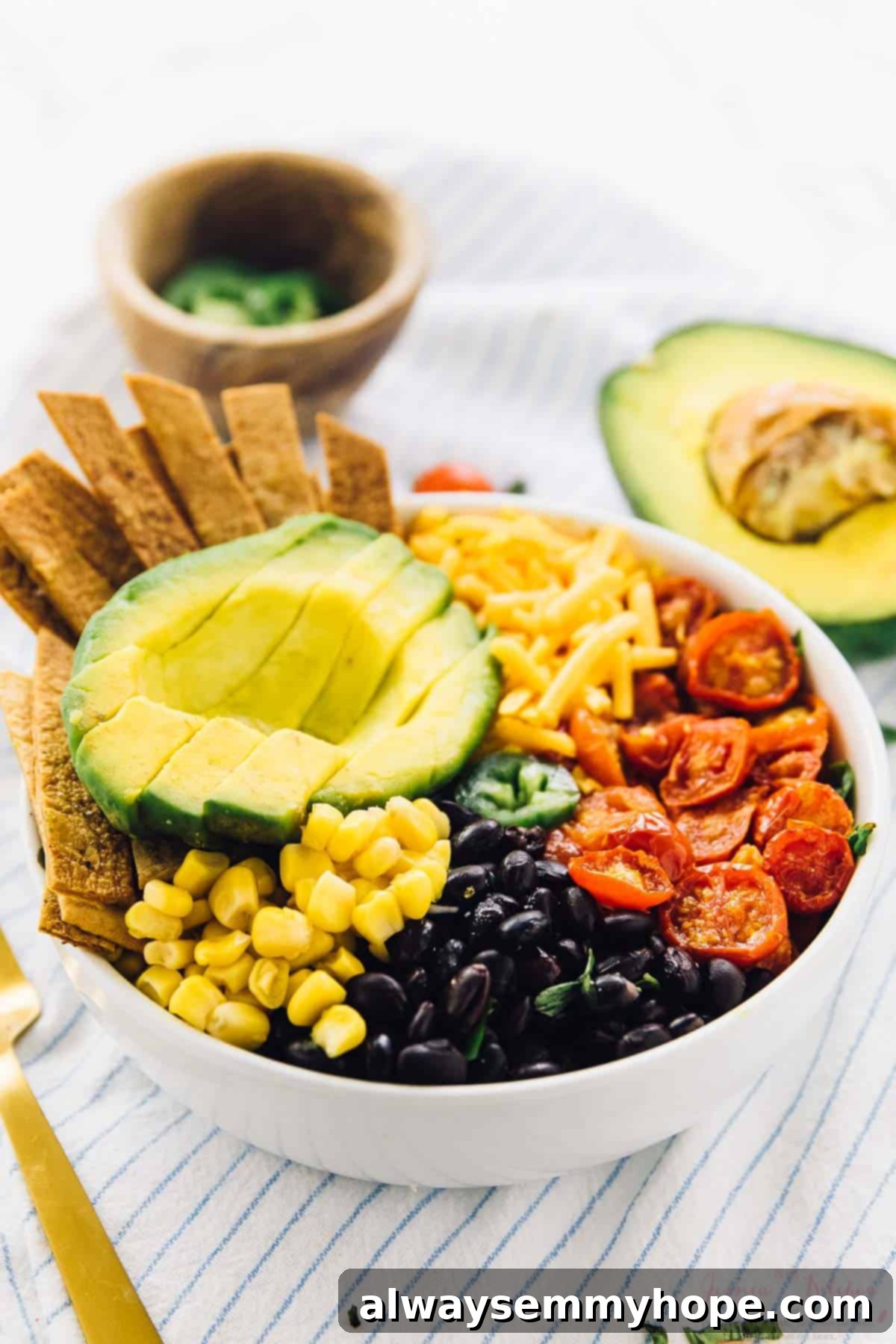Loaded Taco Salad Bowl with Fresh Lime Crema Drizzle 5 Taco salad bowl on a striped cloth with half an avocado in the background.