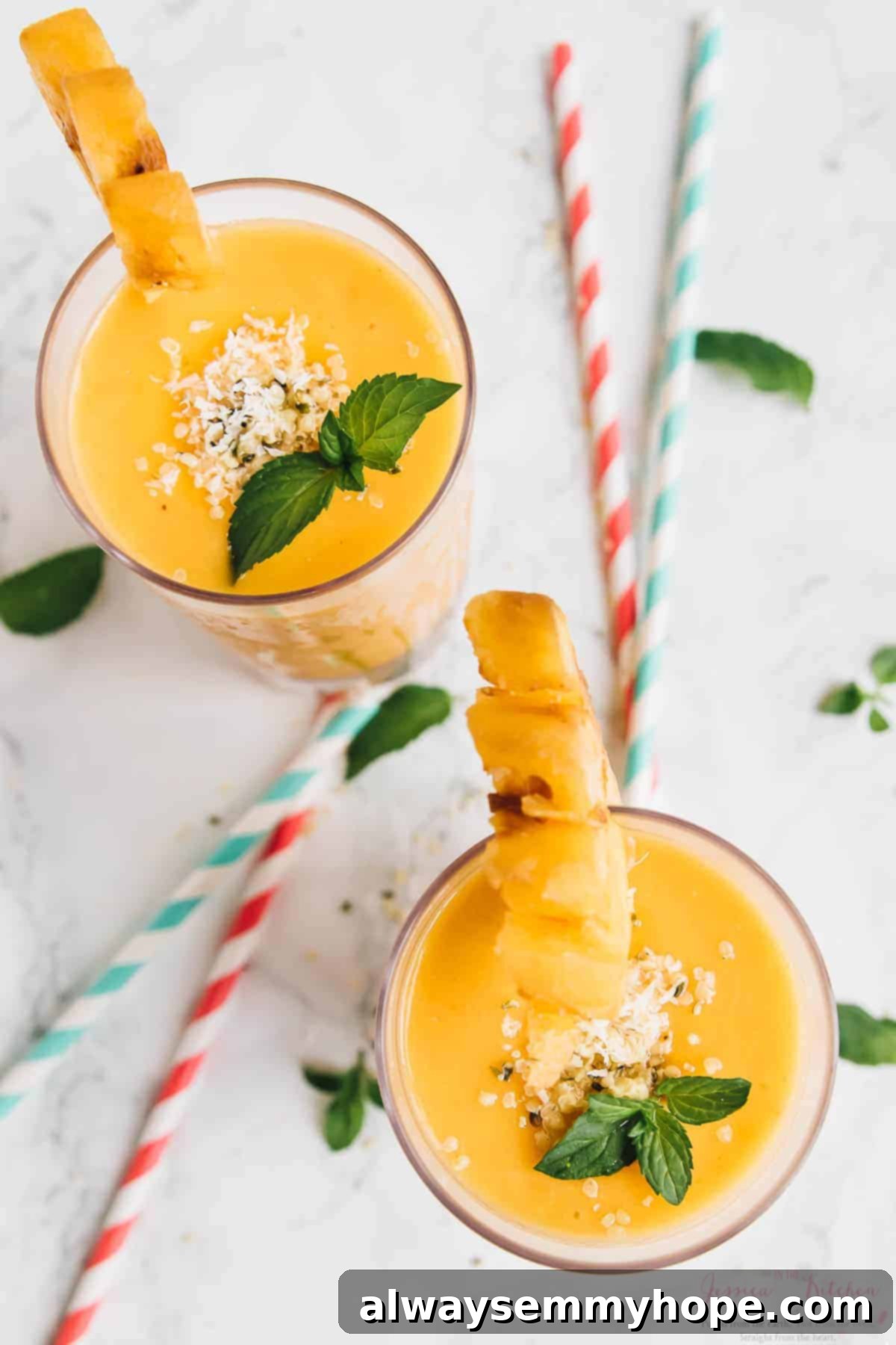 Sunshine Pineapple Peach Smoothie 5 An inviting overhead shot featuring two glasses of pineapple peach smoothies, each with a straw, placed on a wooden surface. A carton of nut milk is visible in the background.