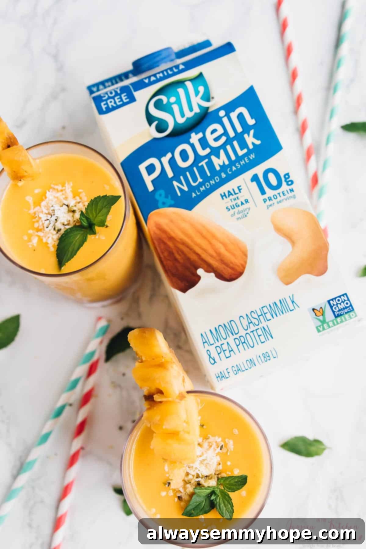 Sunshine Pineapple Peach Smoothie 7 An overhead shot showcasing two pineapple peach smoothies in glasses with straws, positioned next to a carton of Silk Protein Nutmilk on a rustic wooden surface.