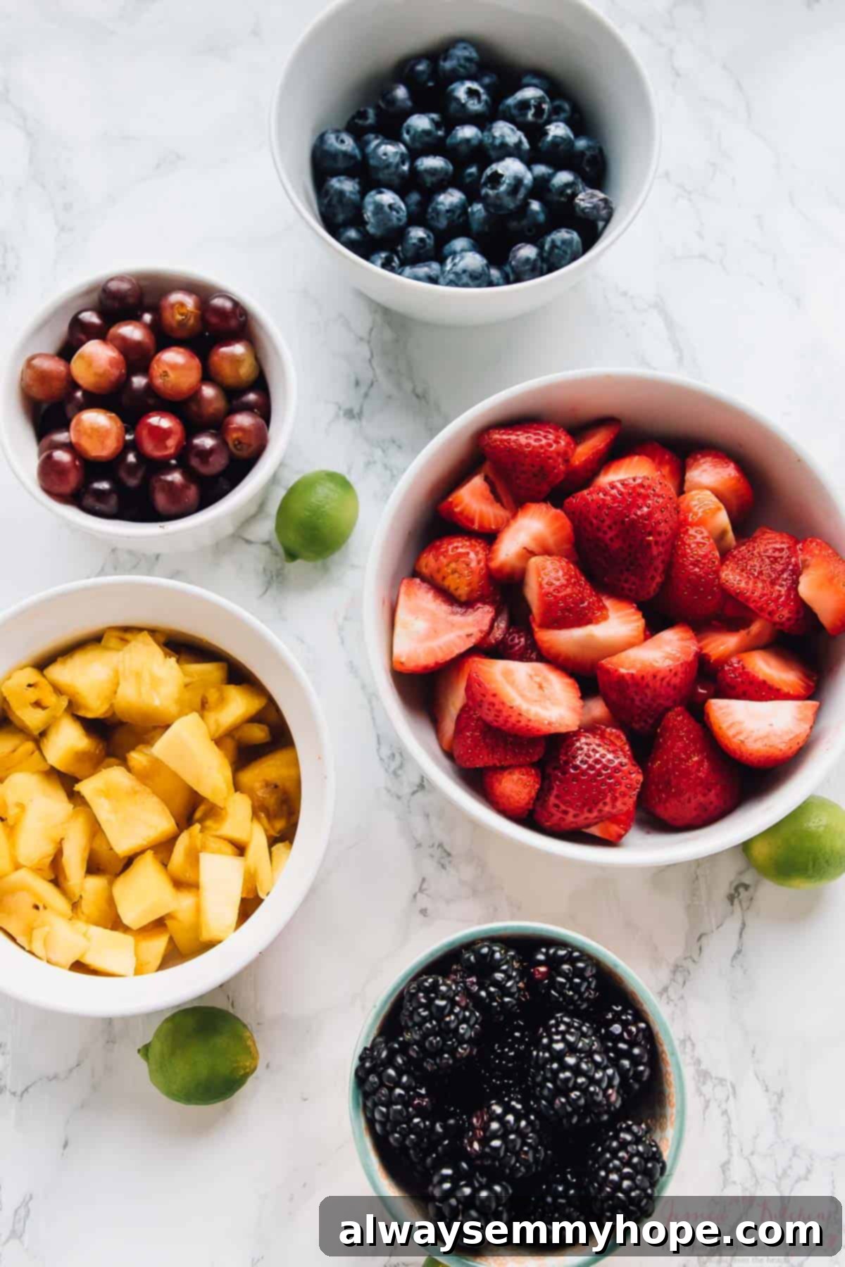Vibrant Fruit Medley with Zesty Maple-Lime Drizzle 3 Overhead view of an assortment of fresh, vibrant fruits meticulously arranged in separate white bowls, ready for preparation.