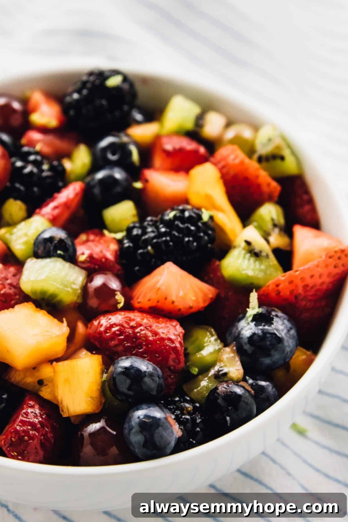 Vibrant Fruit Medley with Zesty Maple-Lime Drizzle 4 Close-up view of the vibrant rainbow fruit salad, perfectly mixed and served in a white bowl, resting on a stylish striped cloth.