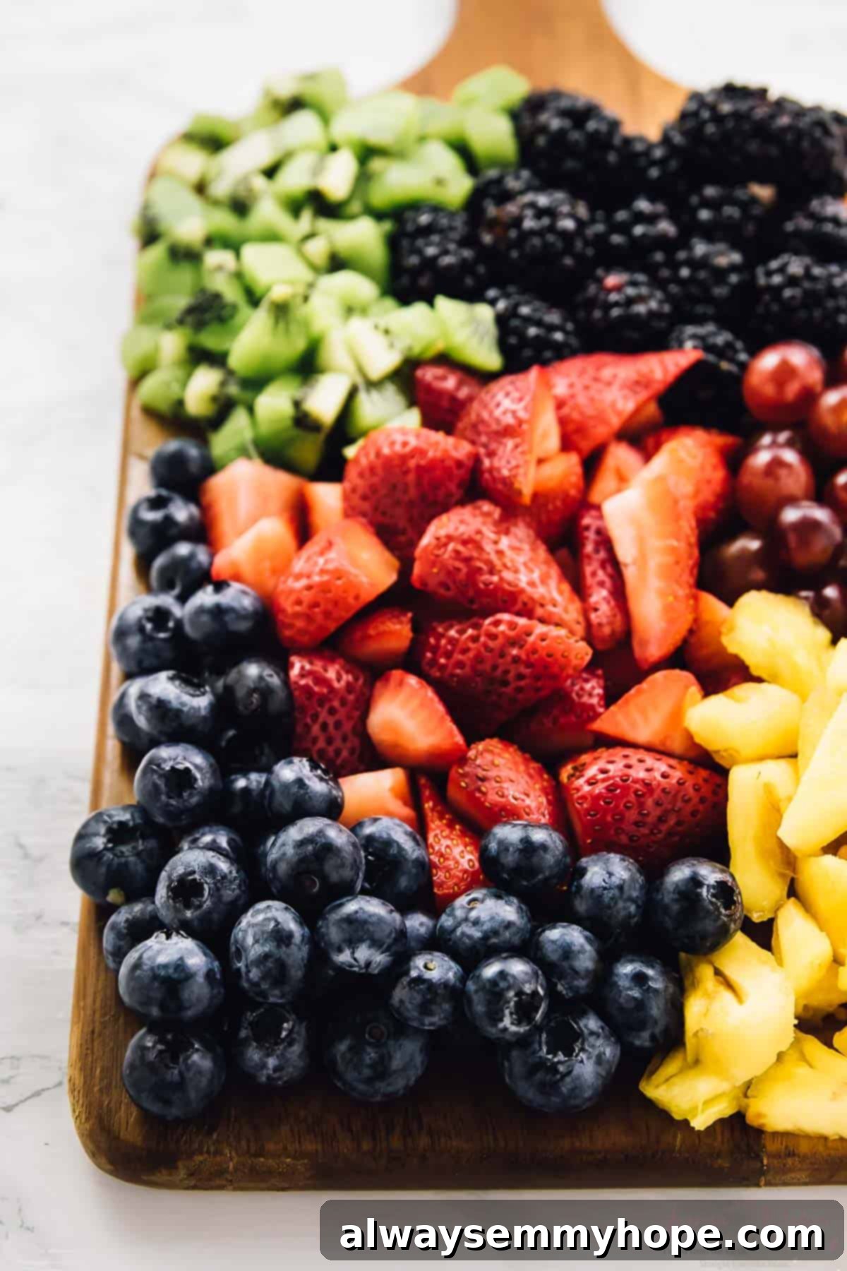 Vibrant Fruit Medley with Zesty Maple-Lime Drizzle 5 A colorful array of chopped strawberries, vibrant kiwi slices, deep purple grapes, golden pineapple chunks, and rich blackberries neatly arranged on a rustic wooden cutting board.