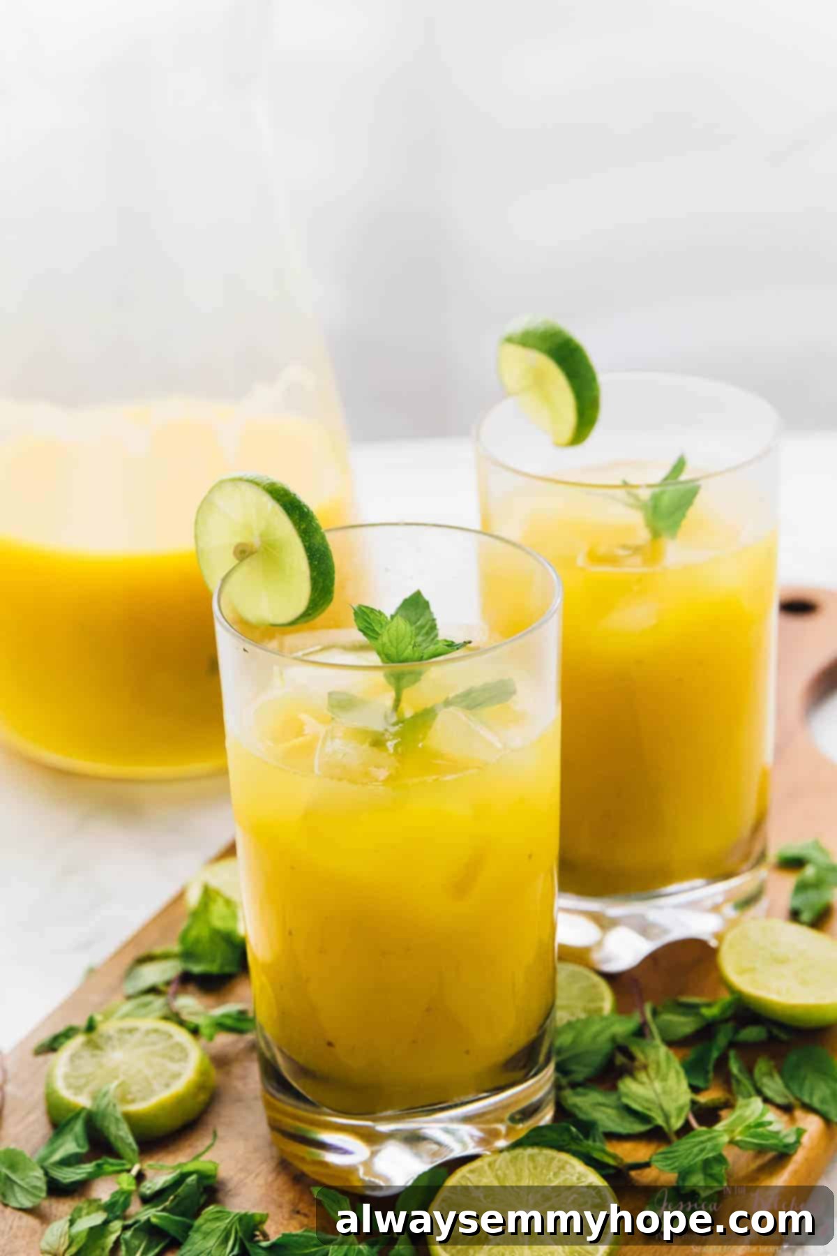 Two glasses of mango mojito on a rustic cutting board, garnished with fresh mint and lime slices, ready for a summer party.