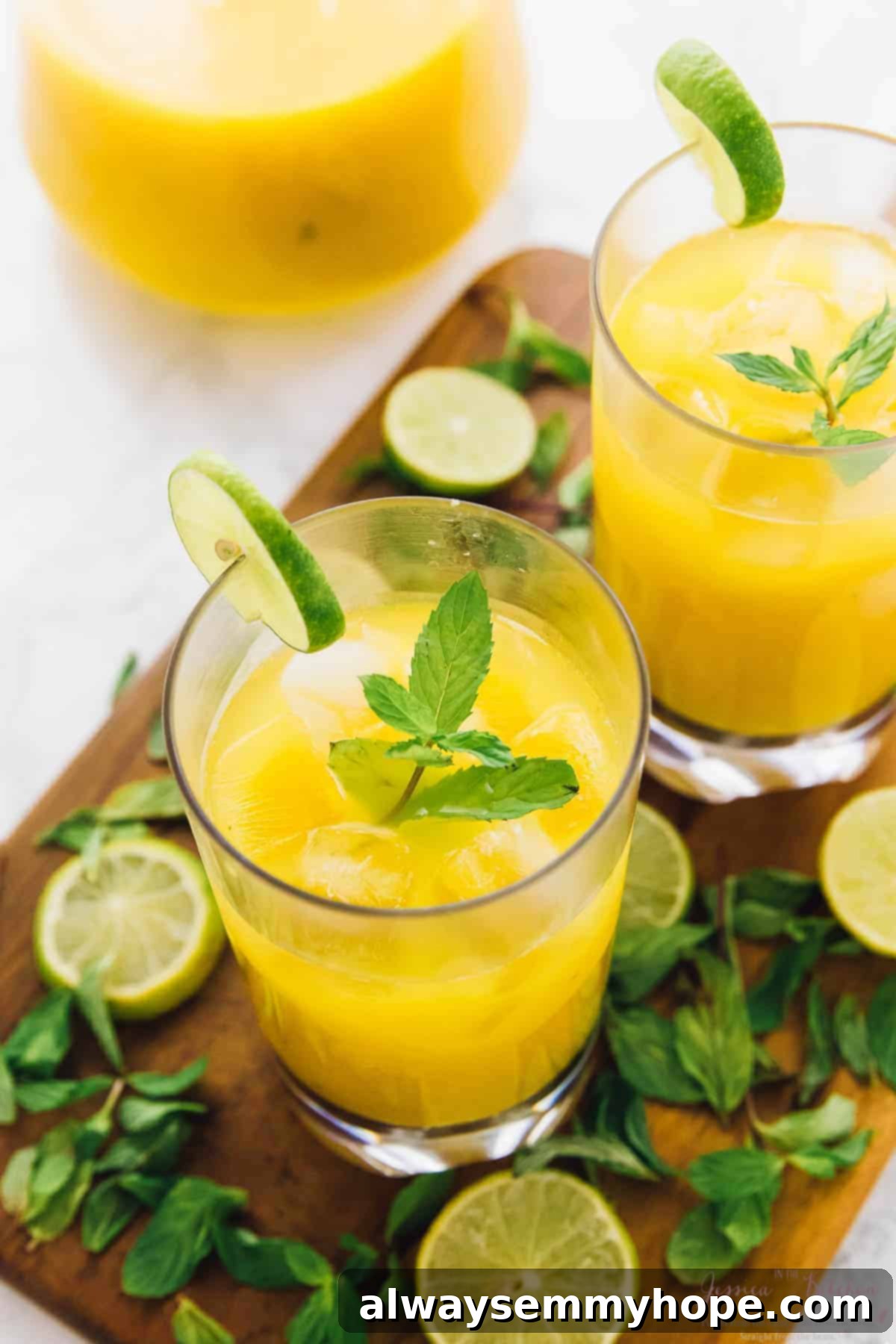 Top-down view of two mango mojitos in glasses on a cutting board, garnished with lime wheels and mint sprigs.