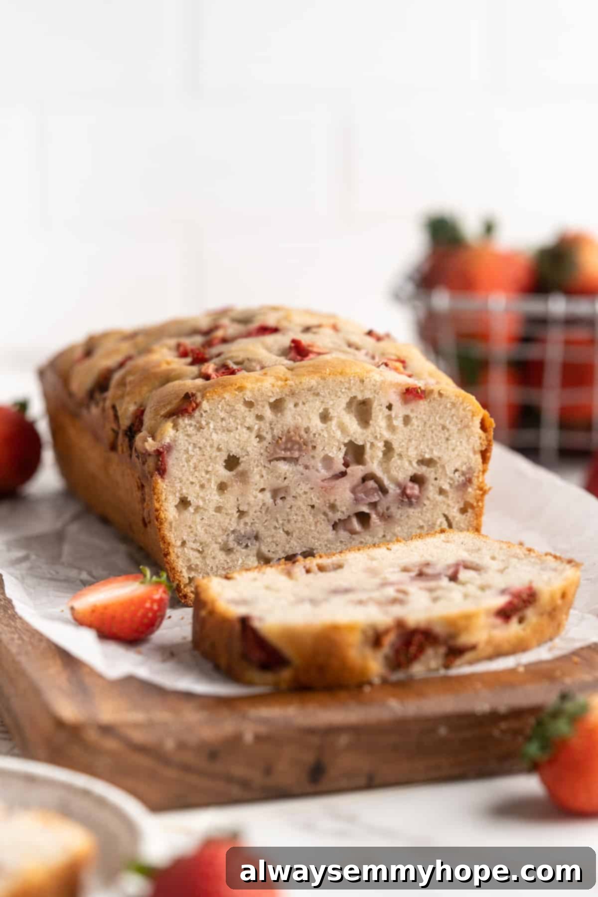 A perfectly baked loaf of gluten-free vegan strawberry banana bread with one slice cut, revealing the moist interior and vibrant strawberries.