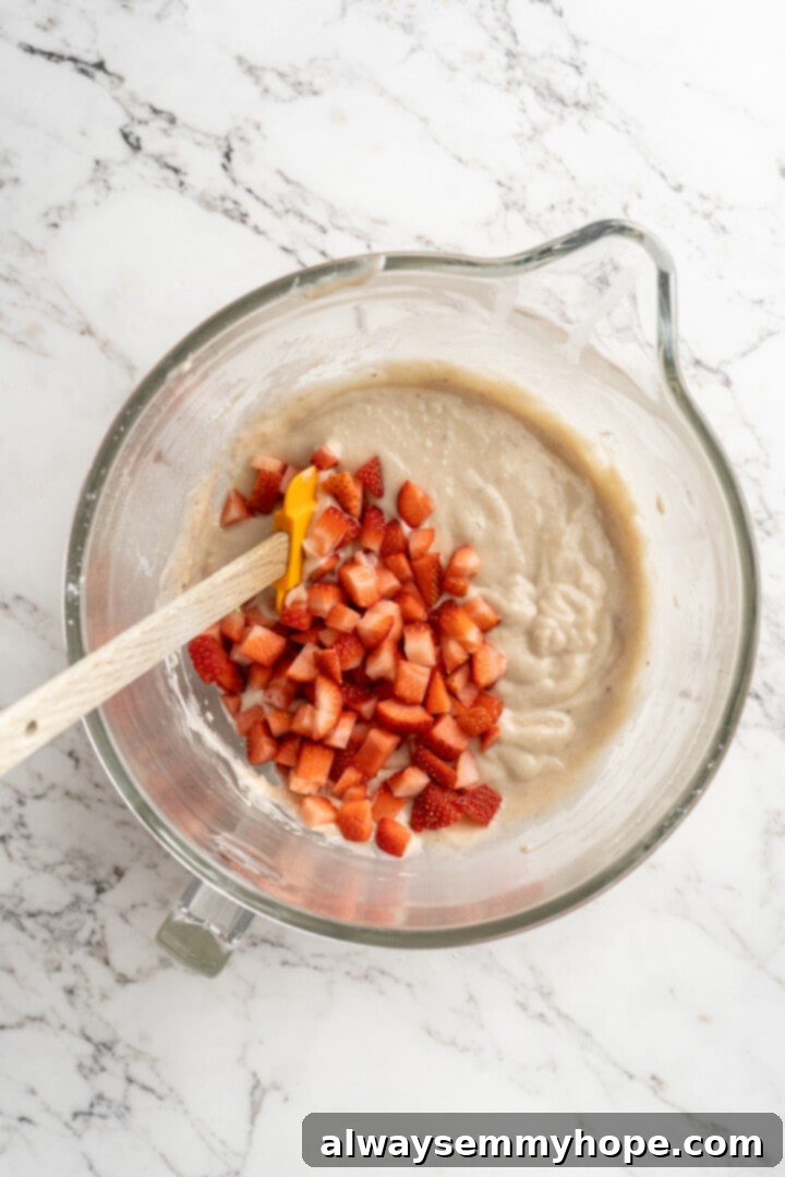 Overhead view of chopped fresh strawberries being folded into the banana bread batter.