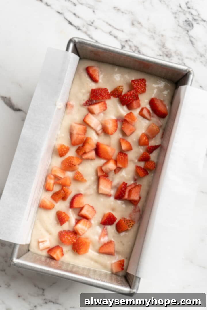 Overhead view of chopped strawberries sprinkled on top of banana bread dough in a loaf pan.