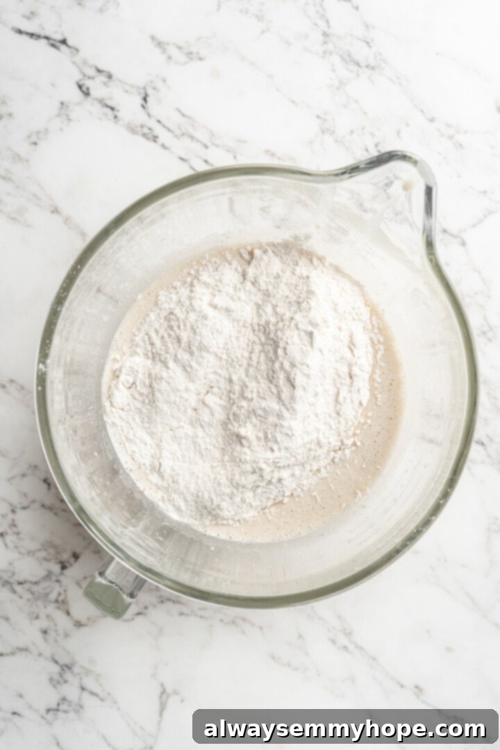 Overhead view of half of the dry ingredients being added to the wet ingredients in a mixer bowl.