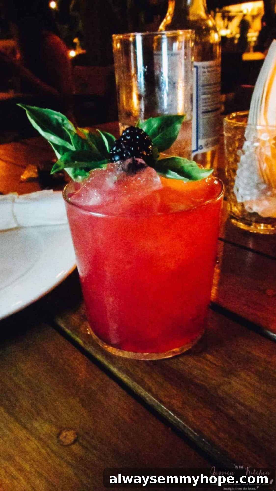 A red cocktail with blackberry garnish, on a wood table. 